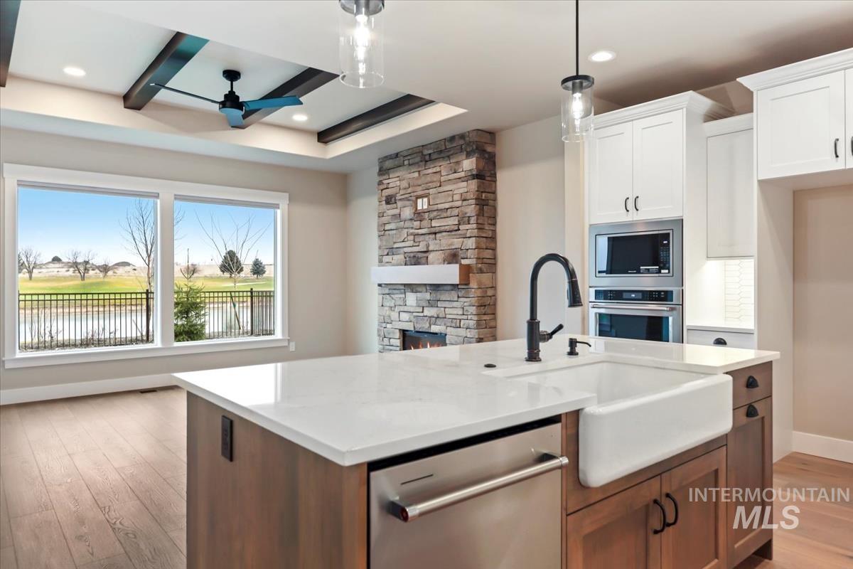 Kitchen with open floor plan, light wood-style flooring, appliances with stainless steel finishes, a kitchen island with sink, and white cabinets