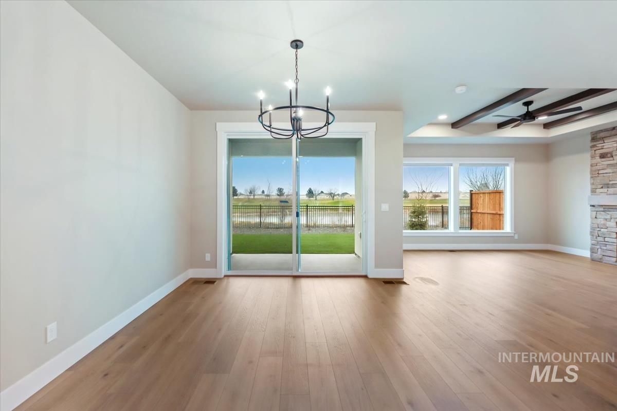 Unfurnished dining area featuring a chandelier, light wood-style floors, a ceiling fan, a water view, and beamed ceiling