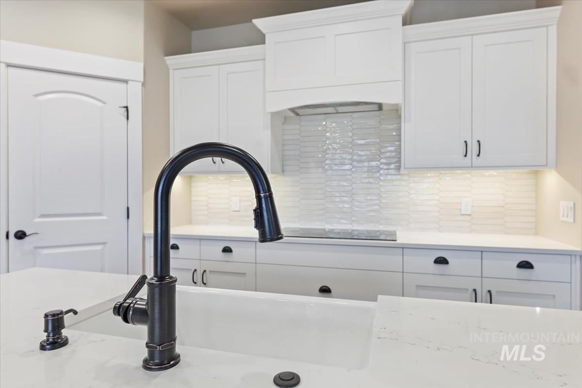 Kitchen with white cabinetry, backsplash, and light stone counters