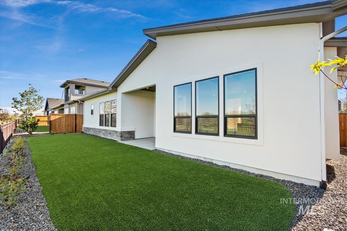 Rear view of house with stucco siding, a fenced backyard, stone siding, and a patio