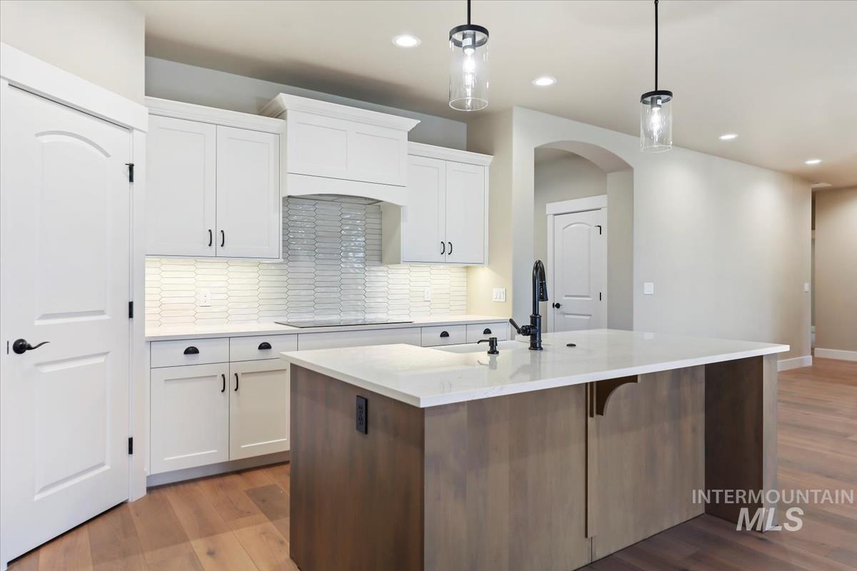 Kitchen featuring white cabinetry, light stone countertops, light wood-type flooring, tasteful backsplash, and an island with sink