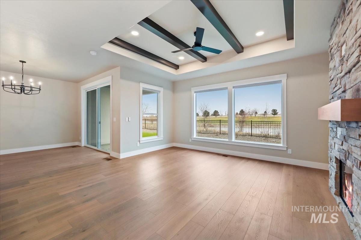 Unfurnished living room featuring a stone fireplace, a tray ceiling, ceiling fan, a chandelier, and light wood-style flooring