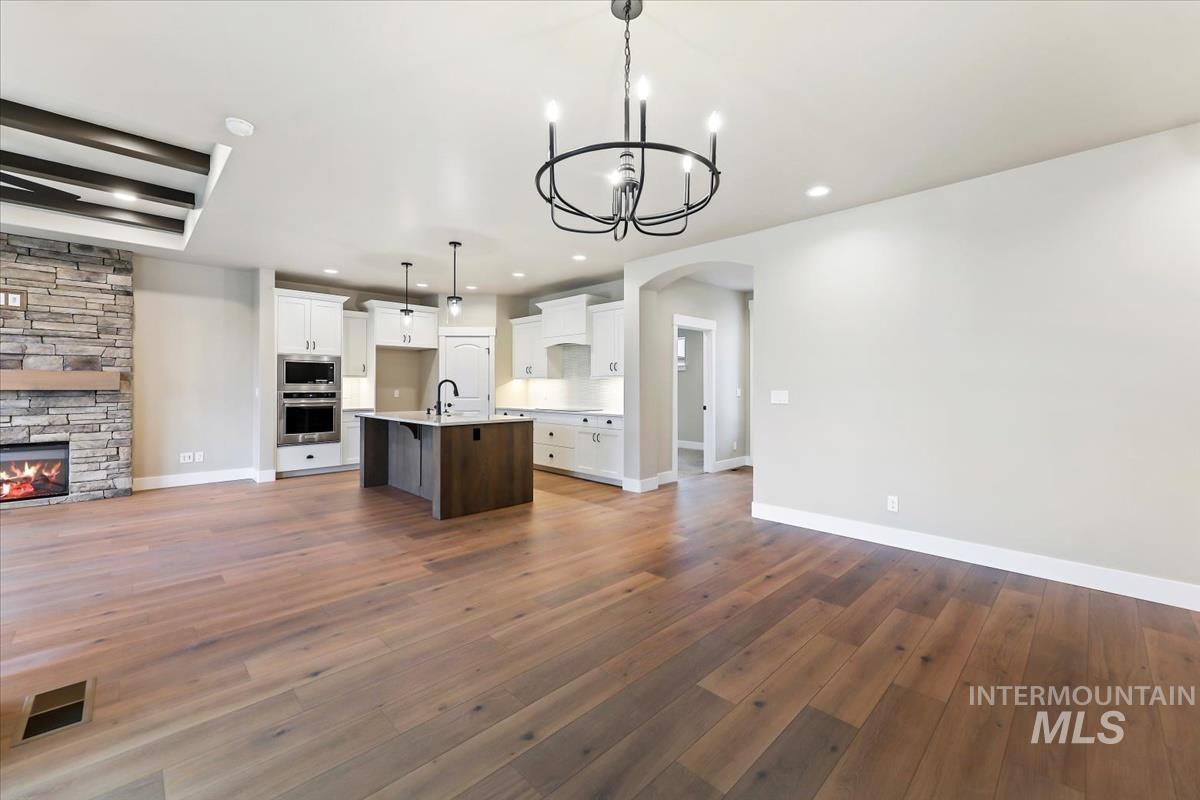 Kitchen featuring open floor plan, arched walkways, white cabinetry, an island with sink, and a fireplace