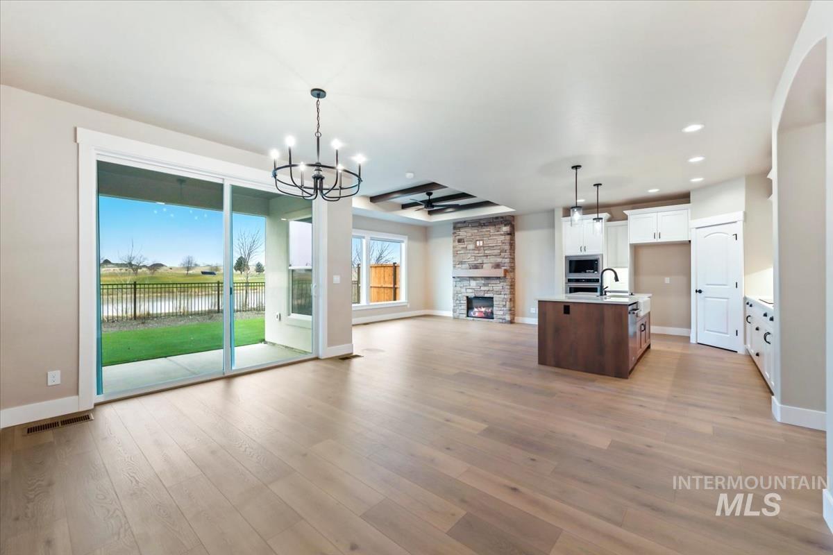 Kitchen featuring open floor plan, a center island with sink, a stone fireplace, hanging light fixtures, and a chandelier