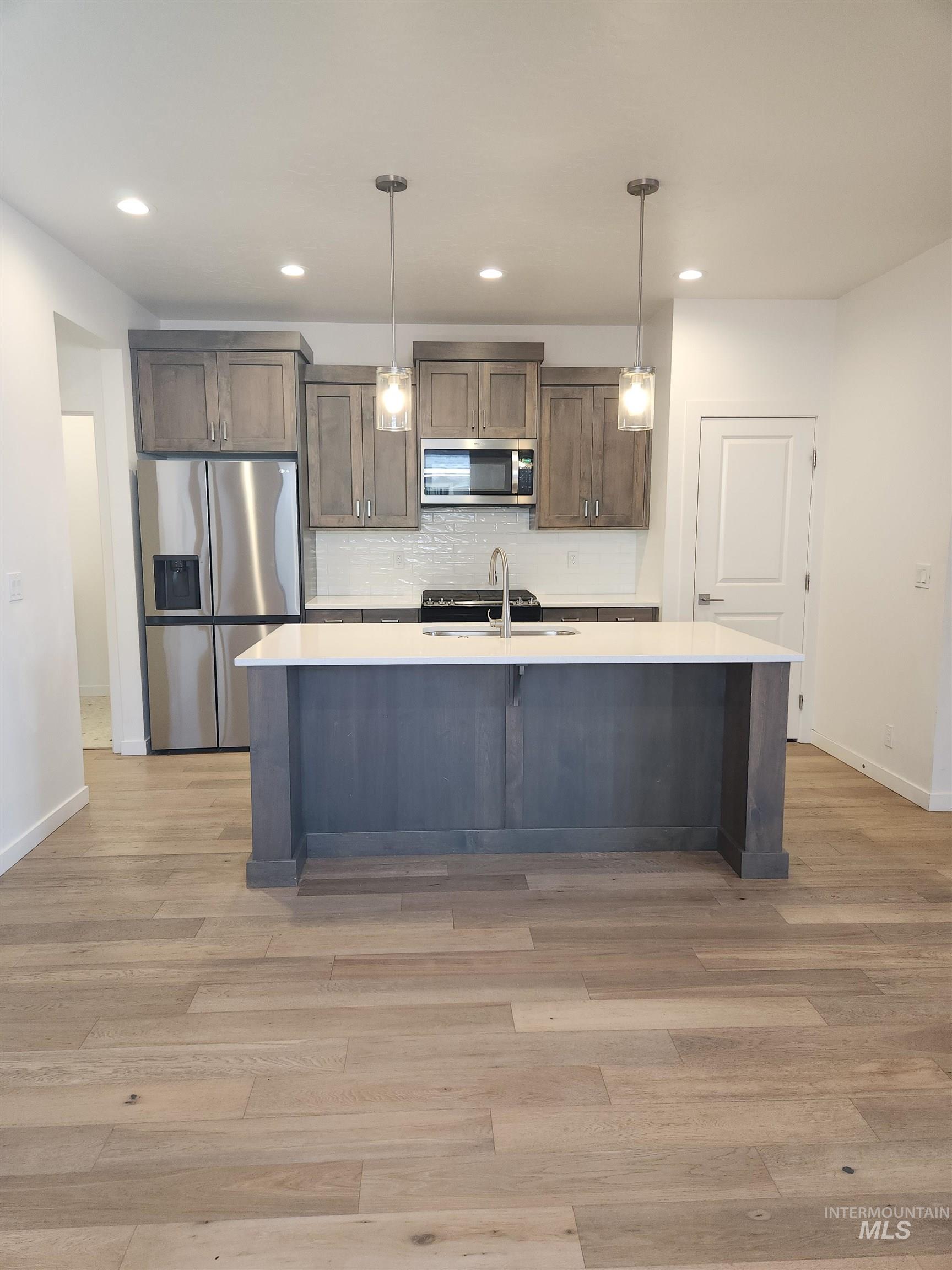 Kitchen featuring stainless steel appliances, decorative light fixtures, backsplash, a kitchen island with sink, and recessed lighting