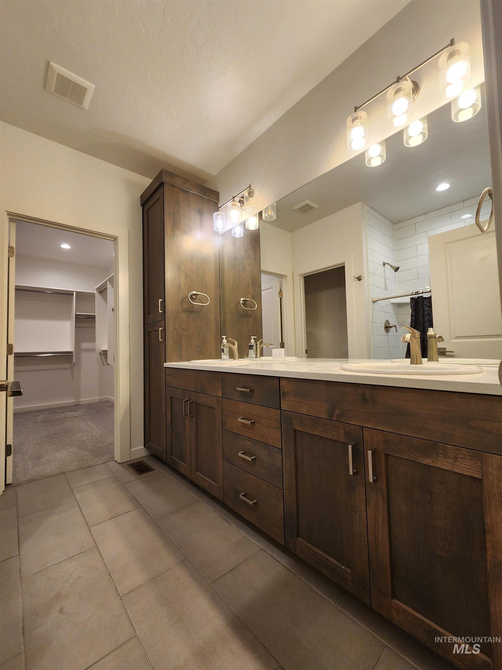 Full bathroom featuring a spacious closet, double vanity, dark tile patterned floors, and recessed lighting