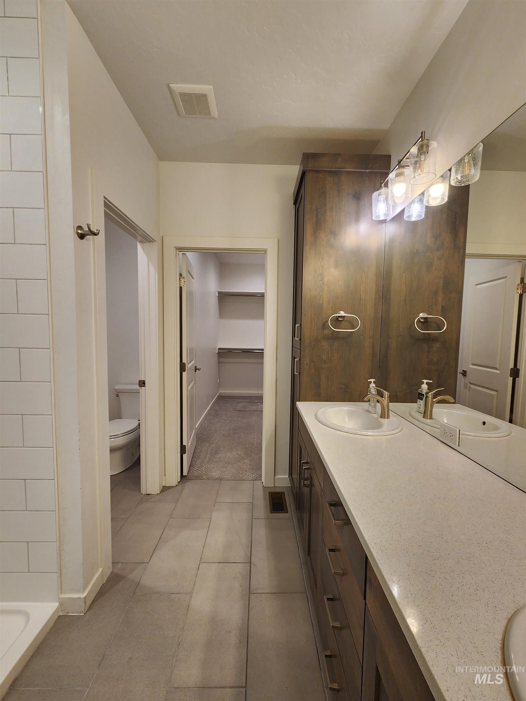 Full bathroom with double vanity, a spacious closet, and a tile shower
