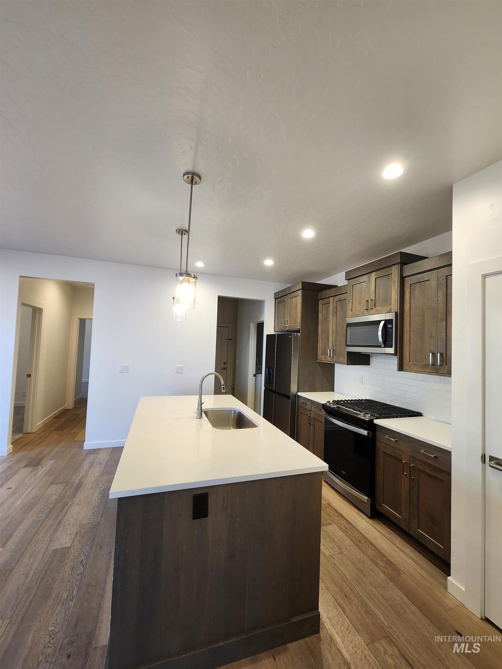 Kitchen with gas stove, dark brown cabinetry, an island with sink, tasteful backsplash, and hanging light fixtures