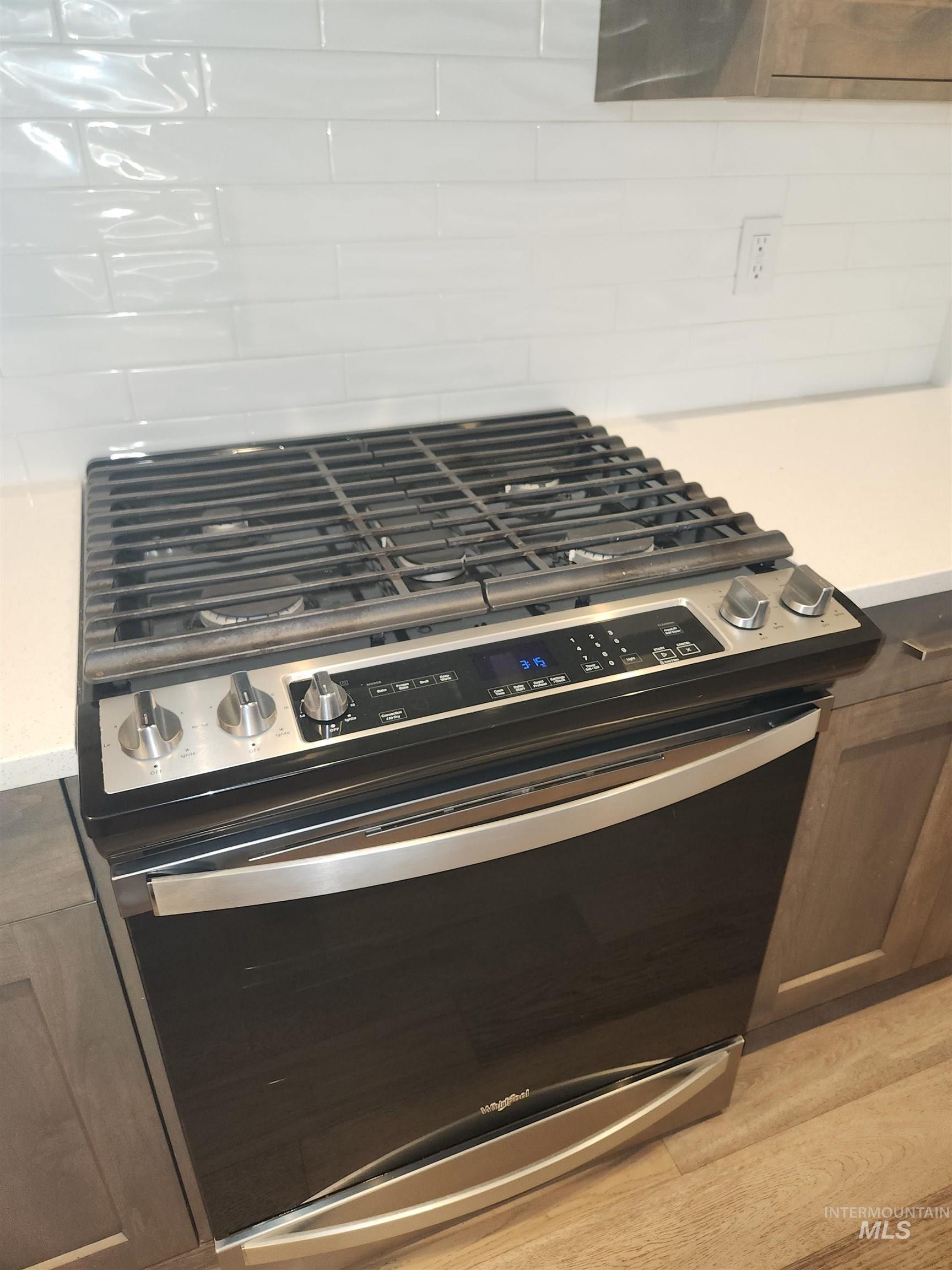 Kitchen view of stainless steel gas range oven, dark brown cabinetry, and light wood finished floors