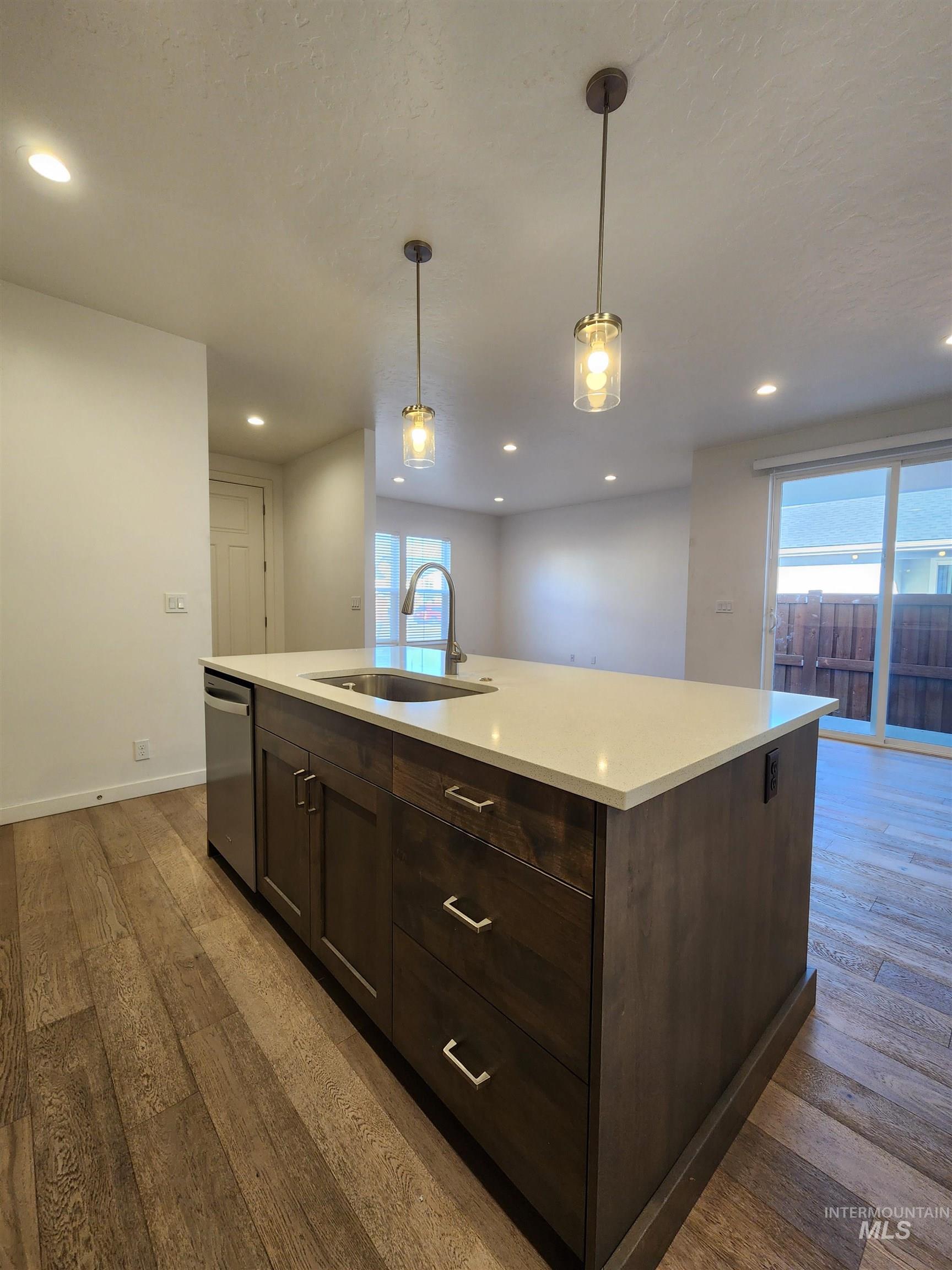 Kitchen featuring dark brown cabinets, an island with sink, pendant lighting, light wood-style flooring, and recessed lighting