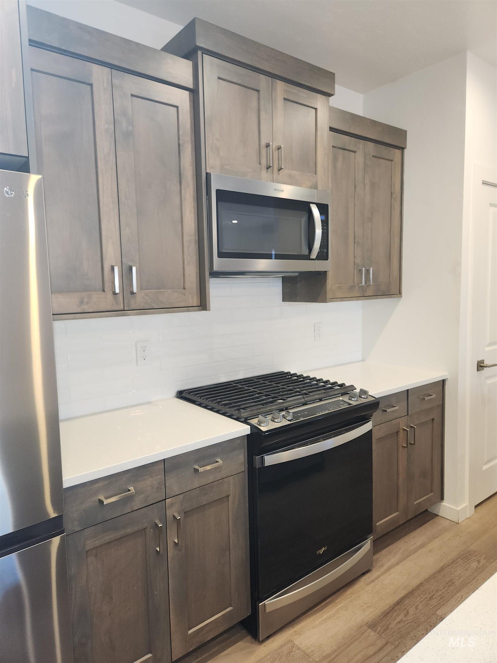 Kitchen with stainless steel appliances, decorative backsplash, light wood finished floors, and dark brown cabinets