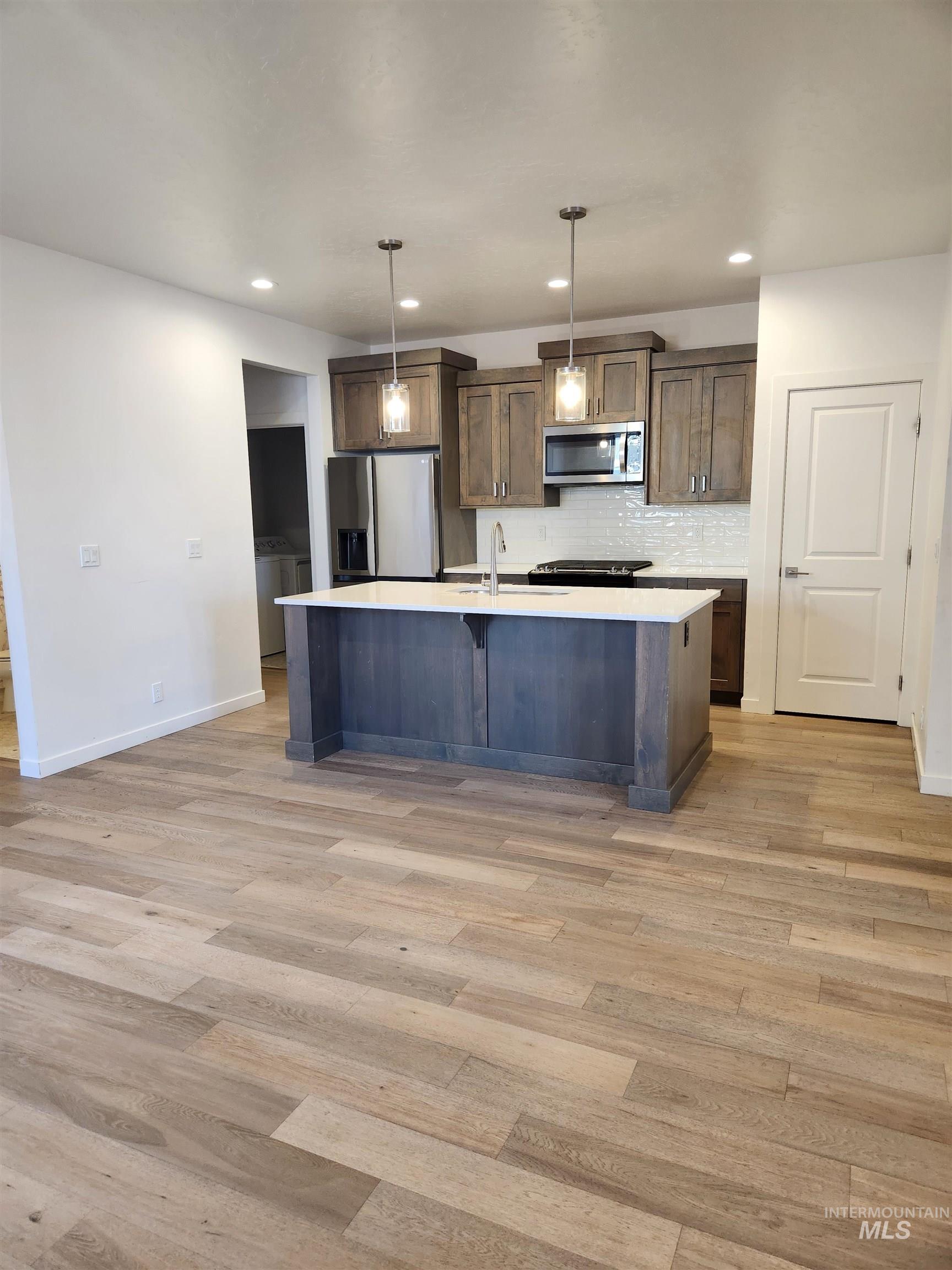 Kitchen with a kitchen bar, backsplash, decorative light fixtures, an island with sink, and appliances with stainless steel finishes