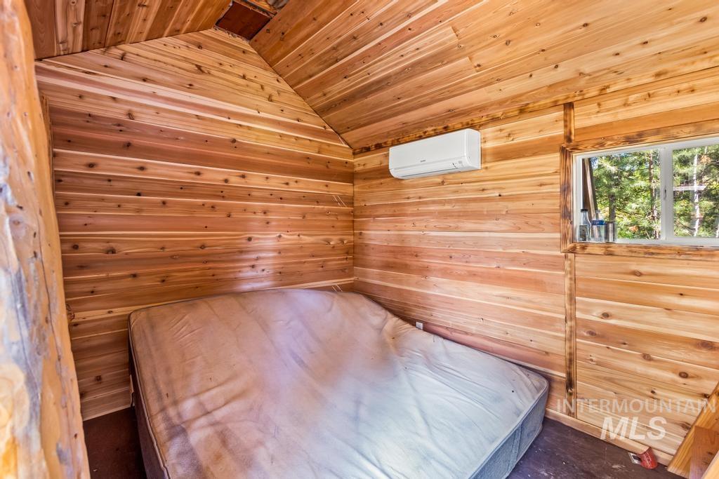 Unfurnished bedroom with a sauna / steam room, lofted ceiling, wood walls, an AC wall unit, and wood ceiling