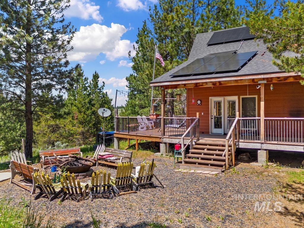 Rear view of house featuring an outdoor fire pit, solar panels, roof with shingles, and a deck