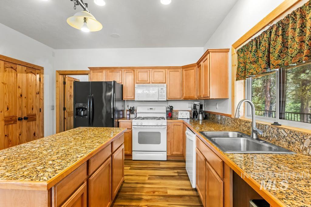 Kitchen featuring white appliances, wood finished floors, decorative light fixtures, brown cabinetry, and a kitchen island