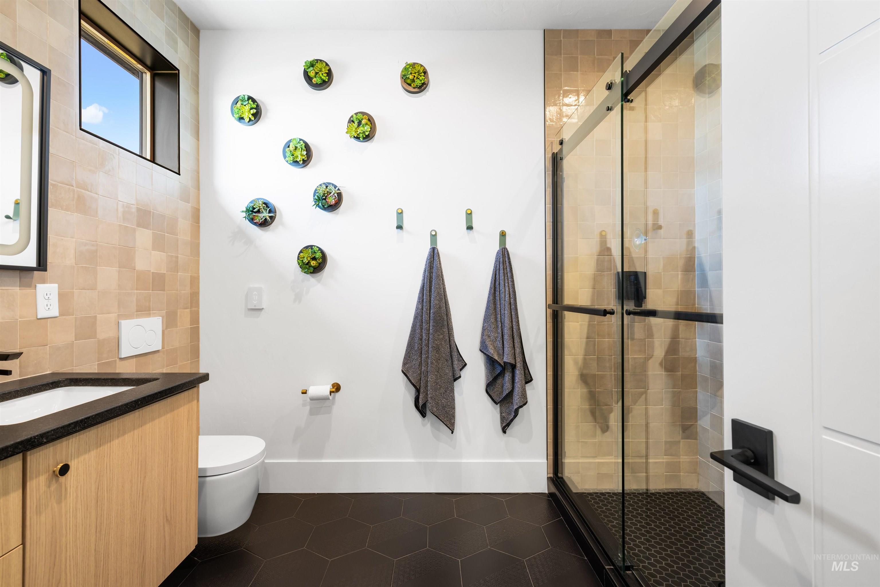 Full bath with vanity, a stall shower, dark tile patterned flooring, tile walls, and tasteful backsplash