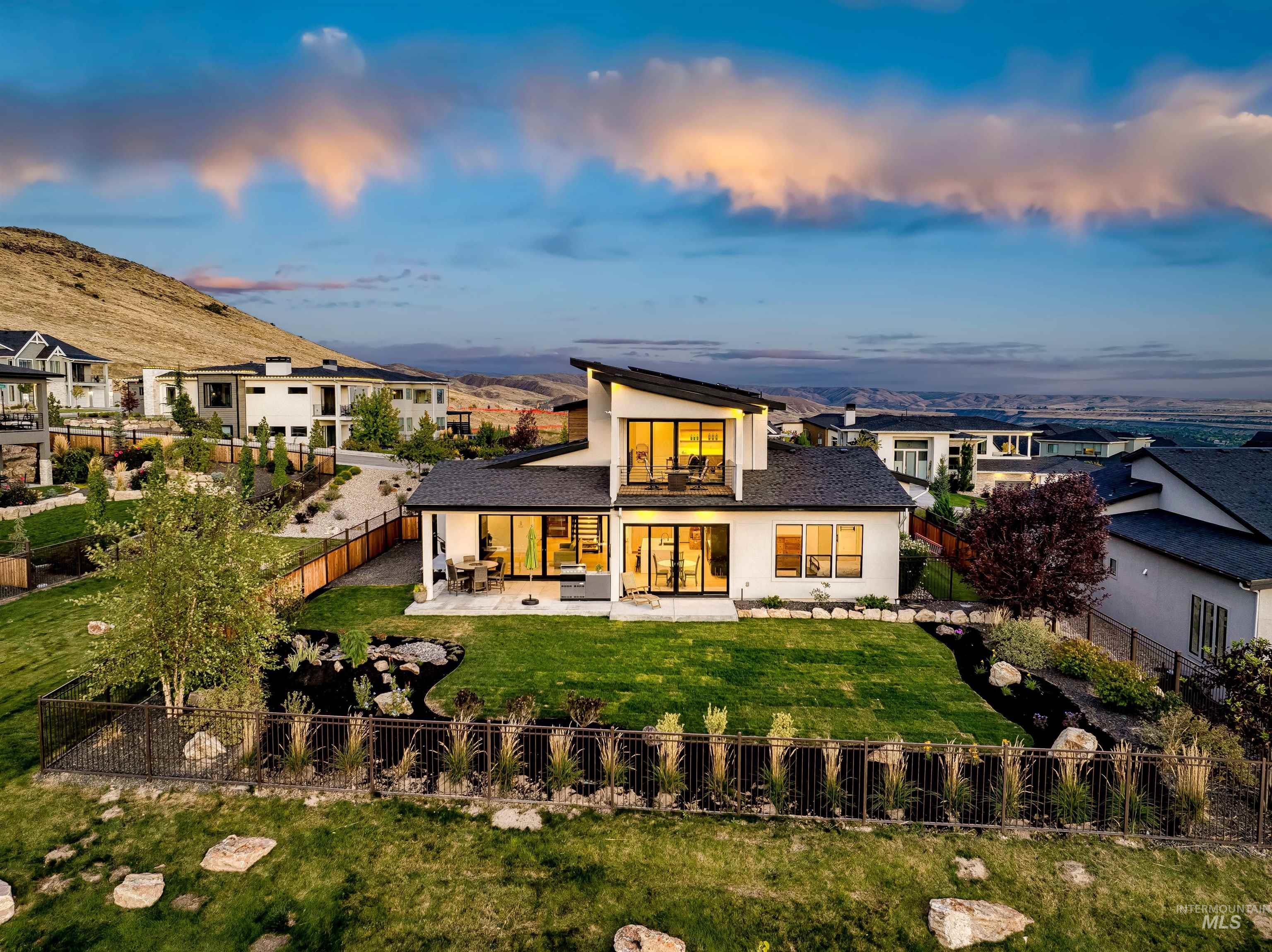 Back of property at dusk featuring a fenced backyard, stucco siding, a patio area, a balcony, and a mountain view