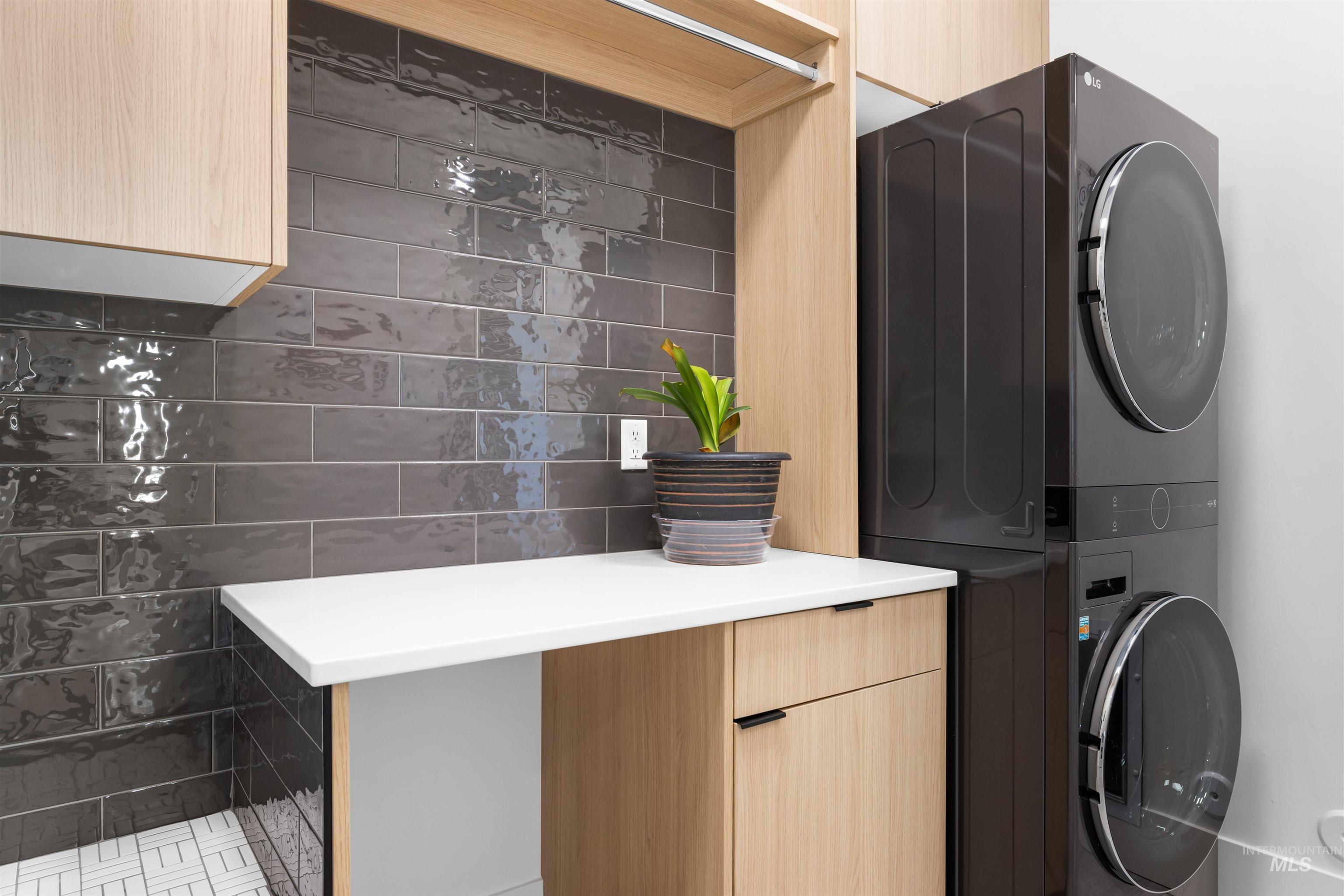 Washroom with stacked washer / drying machine, cabinet space, and tile walls