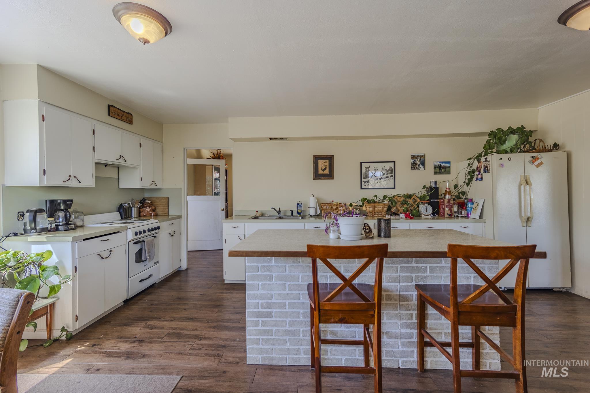 Kitchen featuring light countertops, white appliances, white cabinetry, and a breakfast bar area