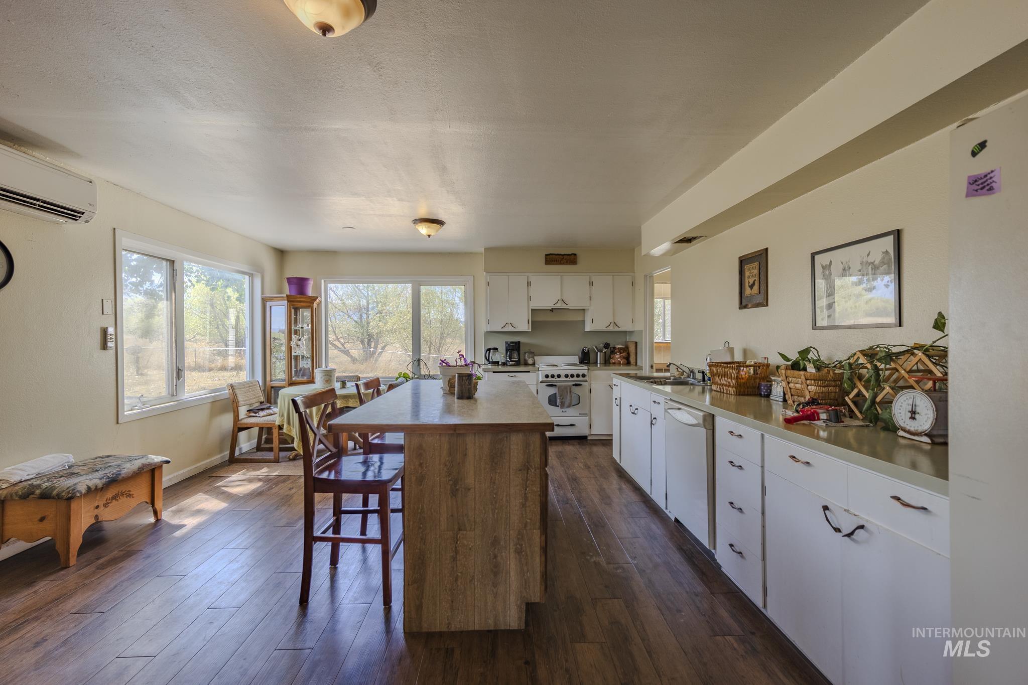 Kitchen with white cabinets, a kitchen island, light countertops, white appliances, and dark wood-type flooring