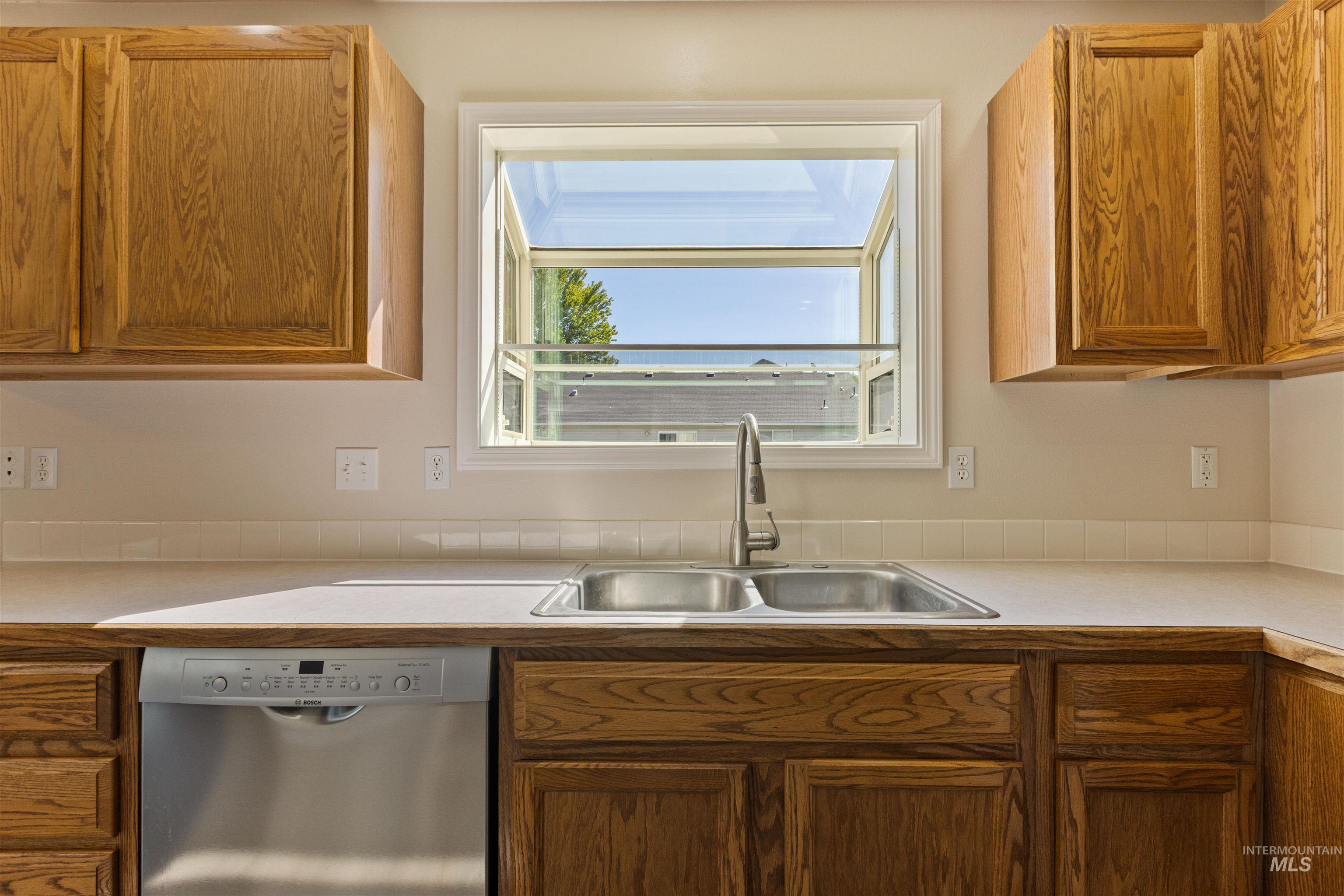 Kitchen with light countertops, dishwasher, and brown cabinetry