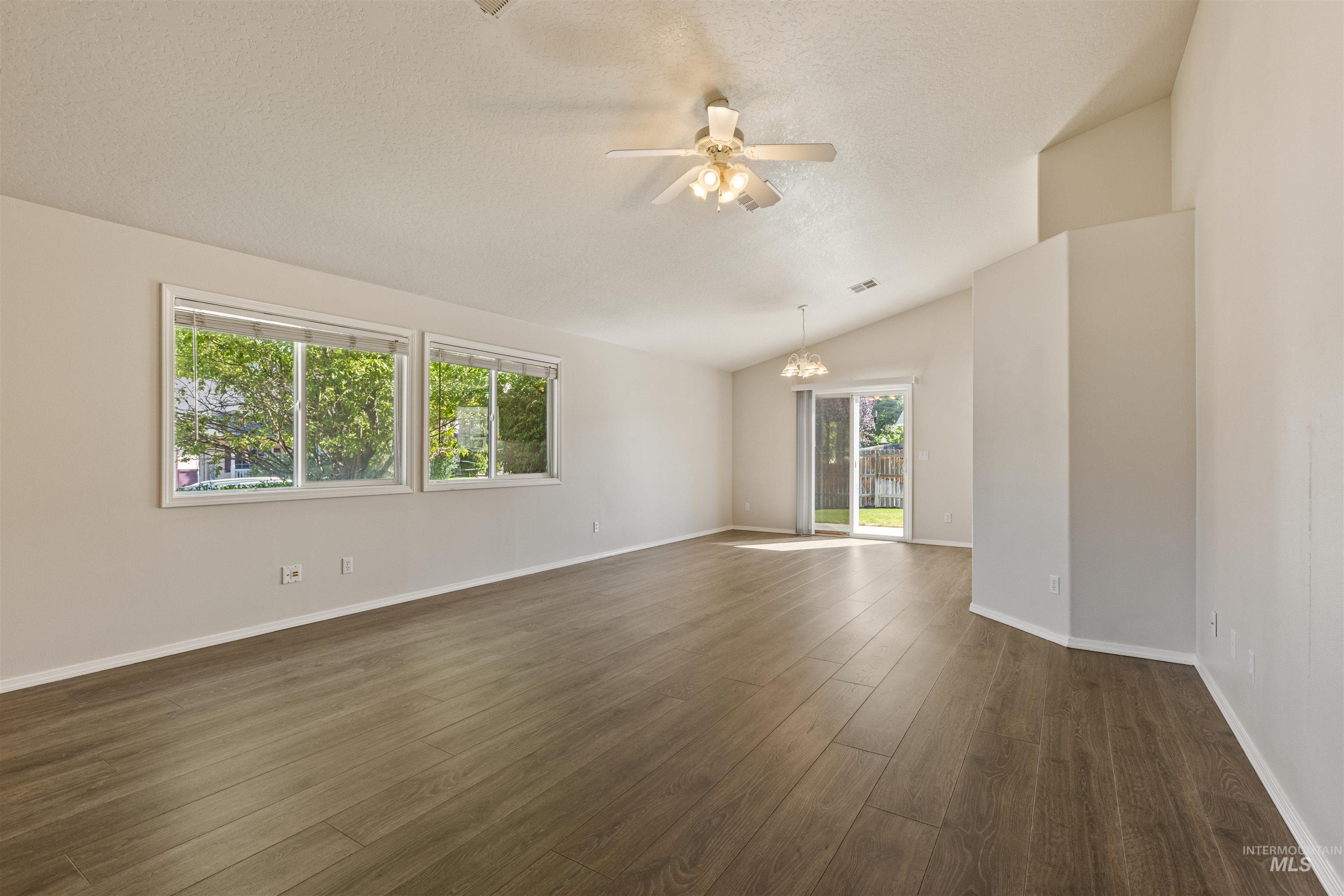 Spare room featuring dark wood-type flooring, vaulted ceiling, a ceiling fan, a textured ceiling, and a chandelier