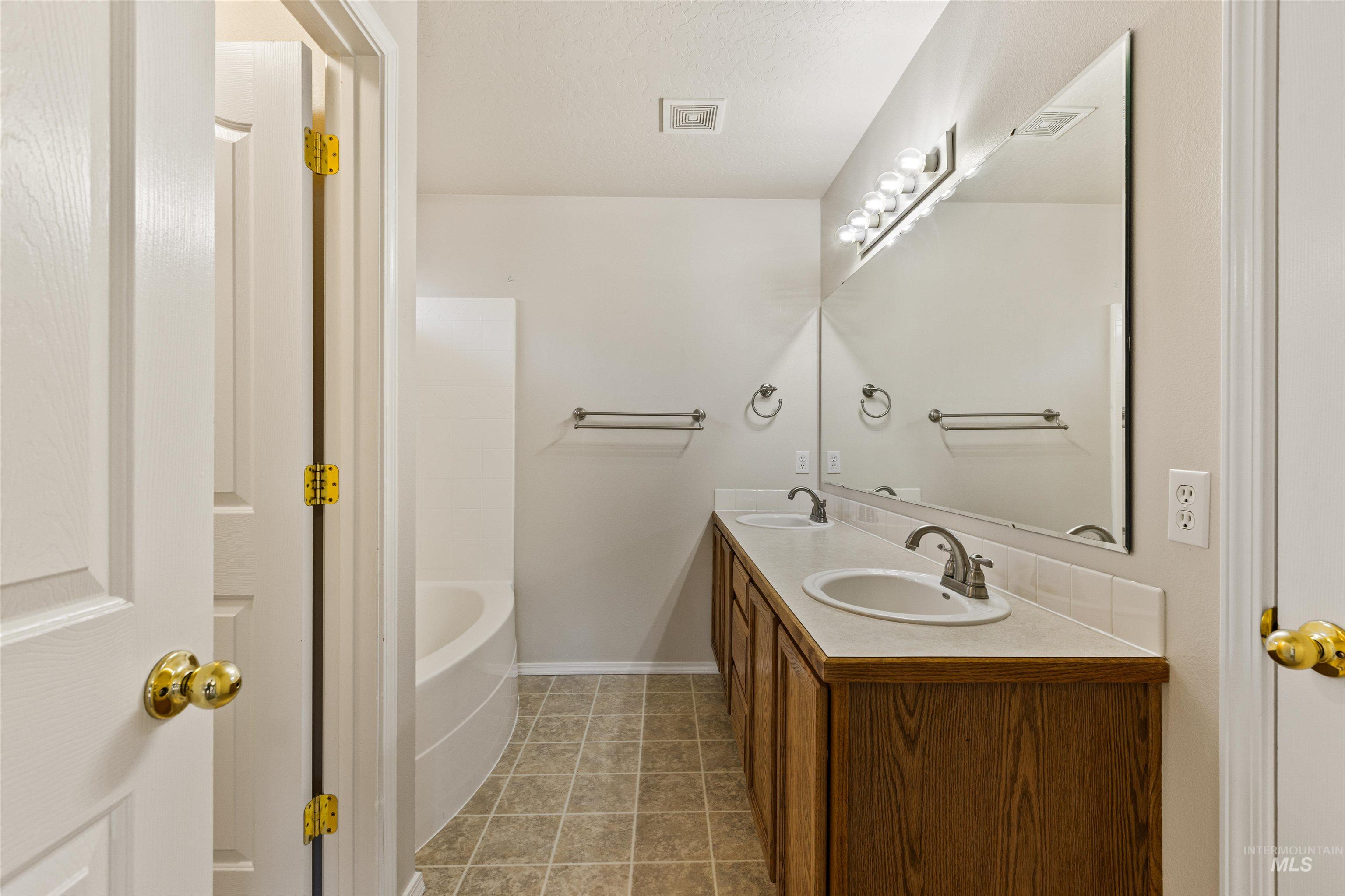 Full bath with a garden tub, light tile patterned floors, and double vanity