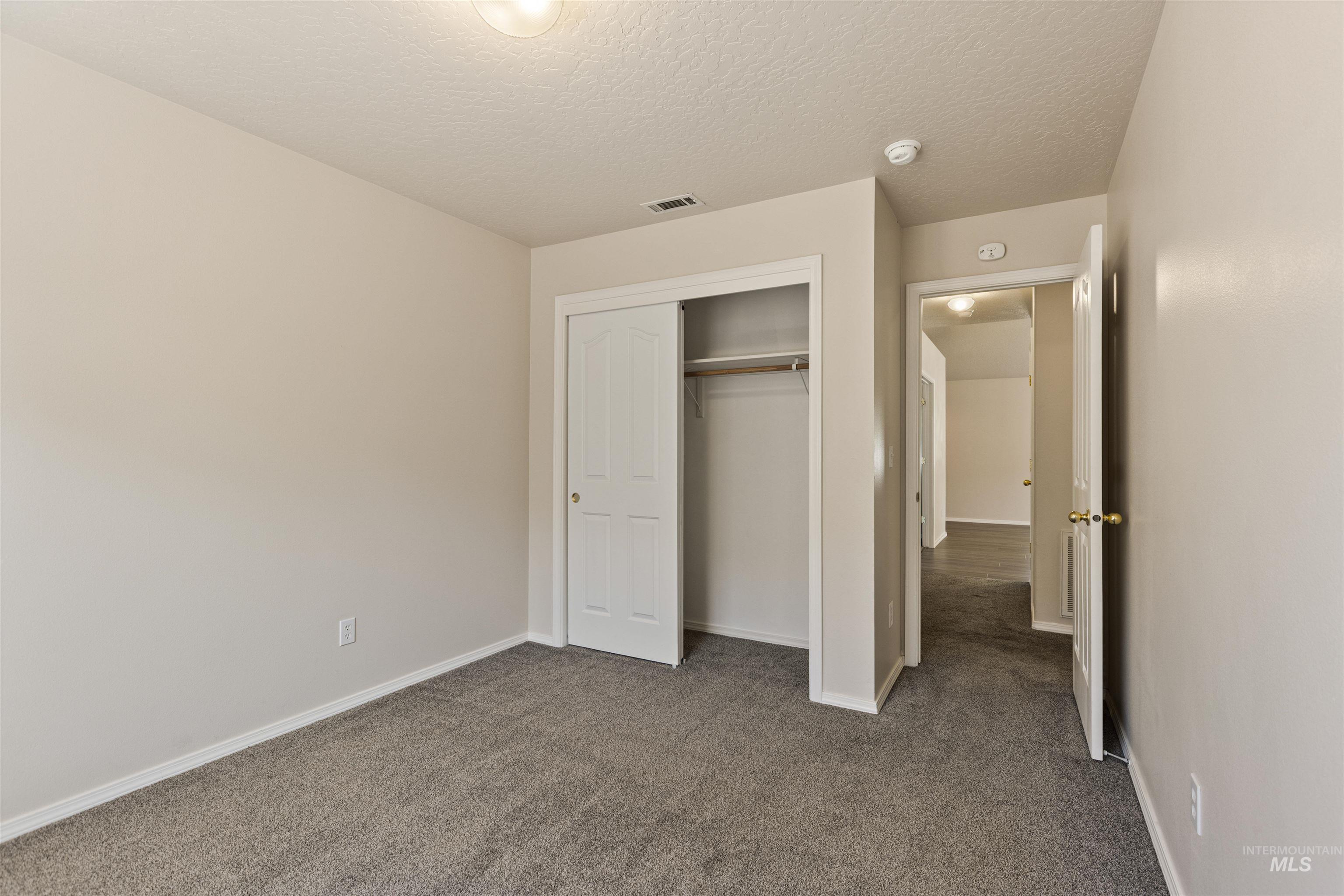 Unfurnished bedroom featuring dark carpet, a textured ceiling, and a closet