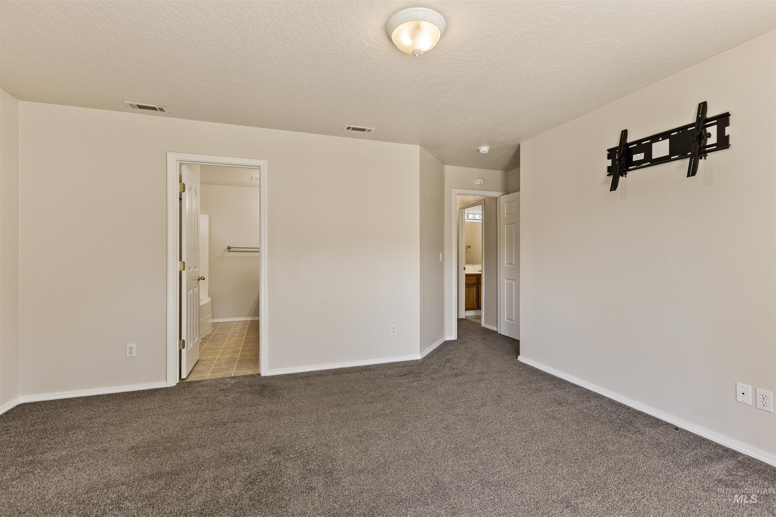 Unfurnished bedroom featuring ensuite bathroom, a textured ceiling, and light colored carpet