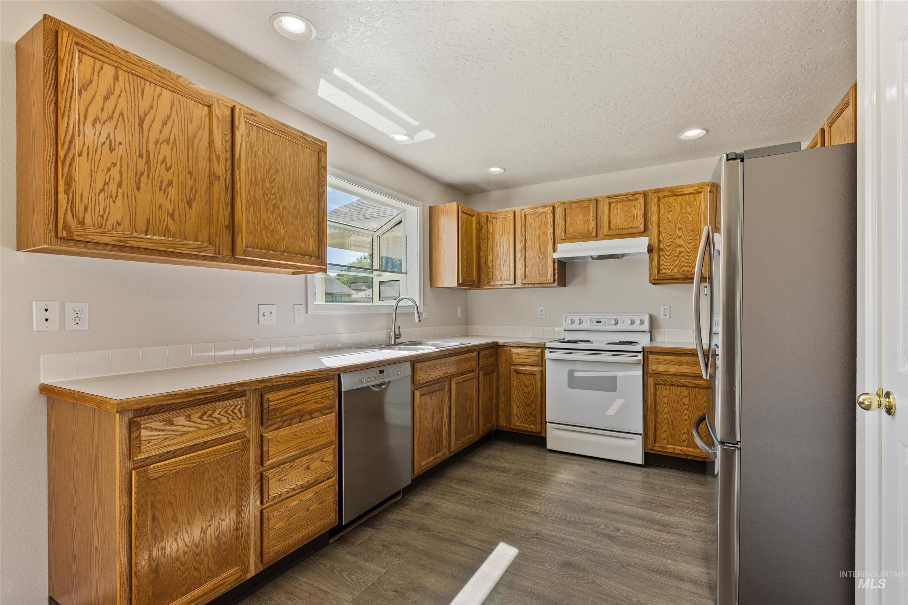 Kitchen with light countertops, stainless steel appliances, recessed lighting, dark wood finished floors, and brown cabinetry