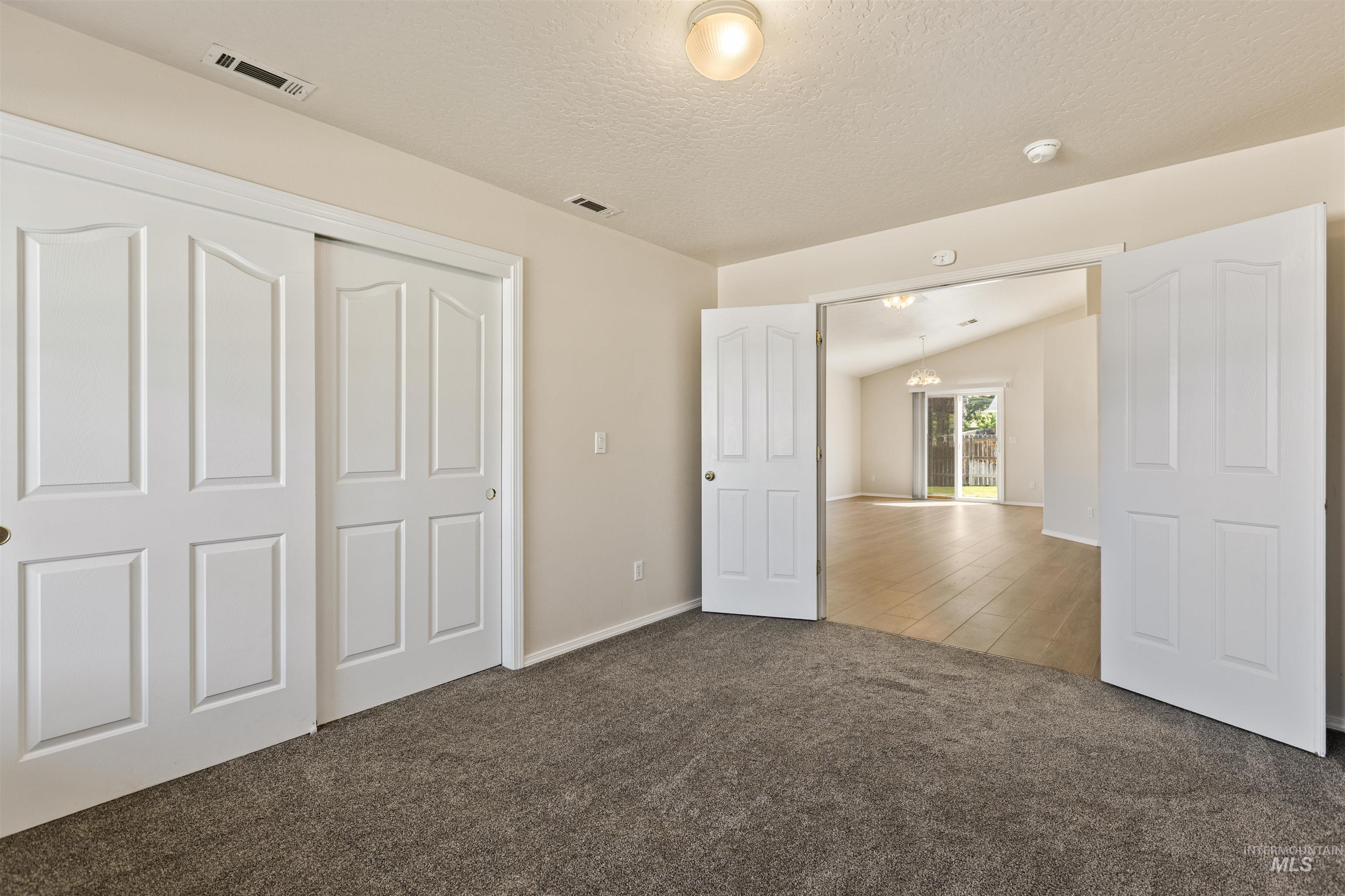 Unfurnished bedroom featuring carpet flooring, a closet, a textured ceiling, a chandelier, and lofted ceiling