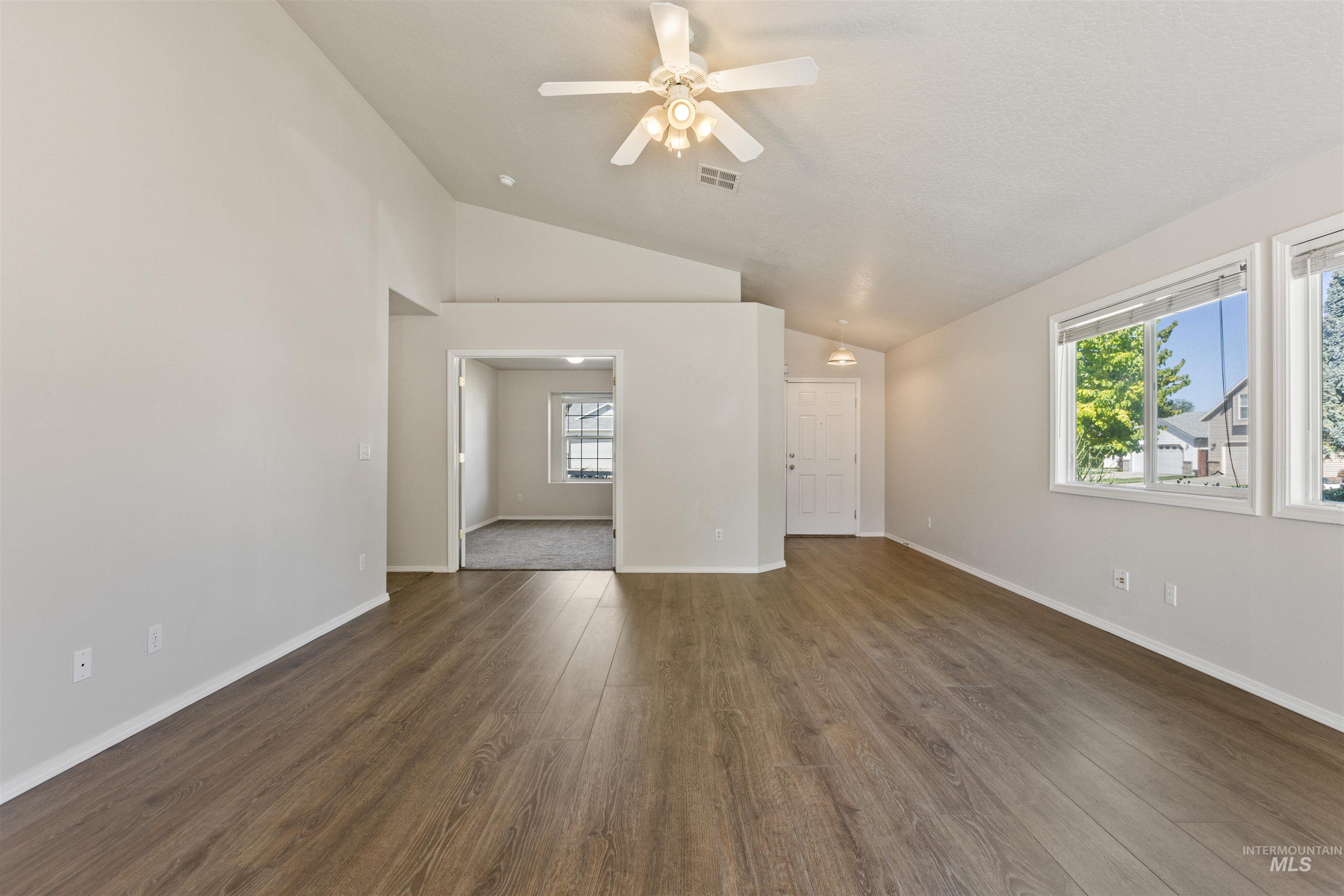 Unfurnished living room featuring dark wood-style floors, lofted ceiling, and a ceiling fan