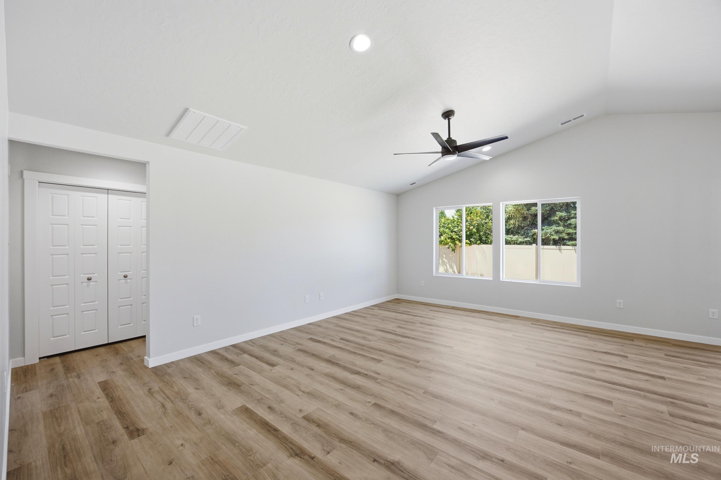 Spacious room featuring wood-finish flooring, vaulted ceilings, and a contemporary ceiling fan
