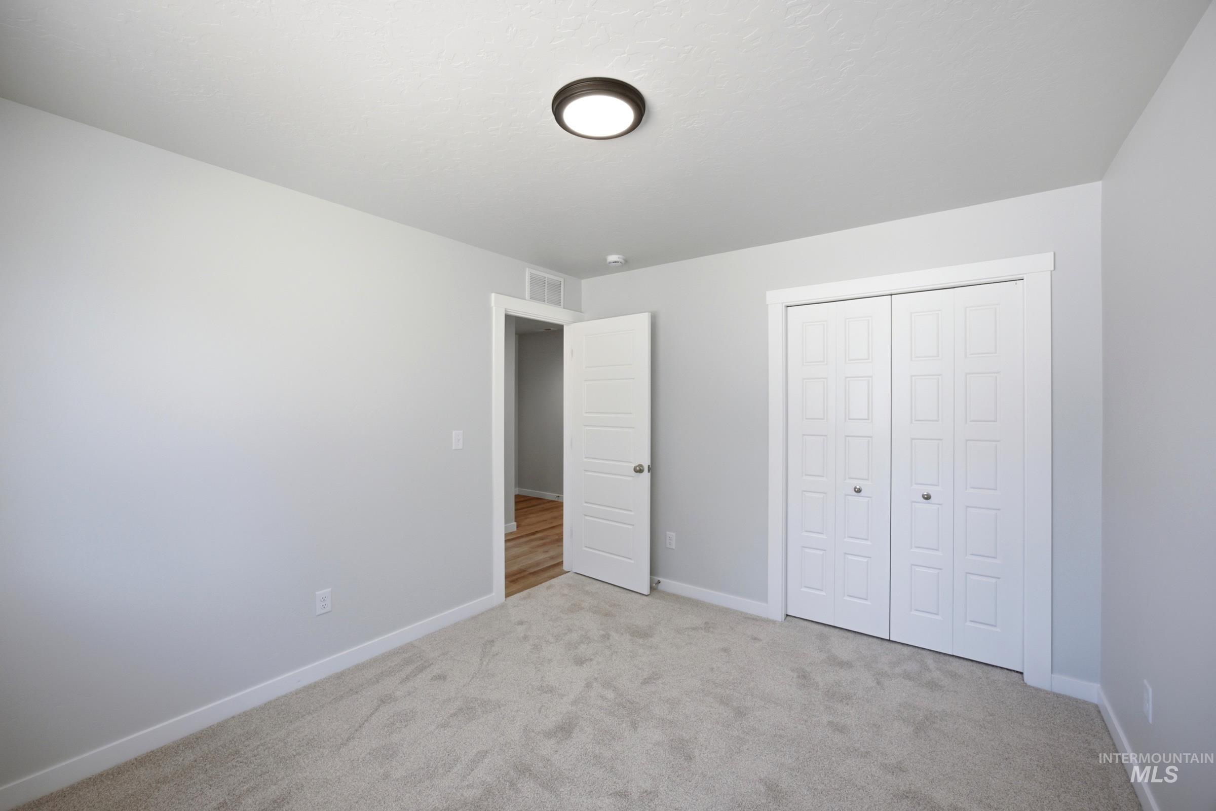 Carpeted room featuring light gray wall paint, a ceiling-mounted light fixture, white bi-fold closet doors, and white trim