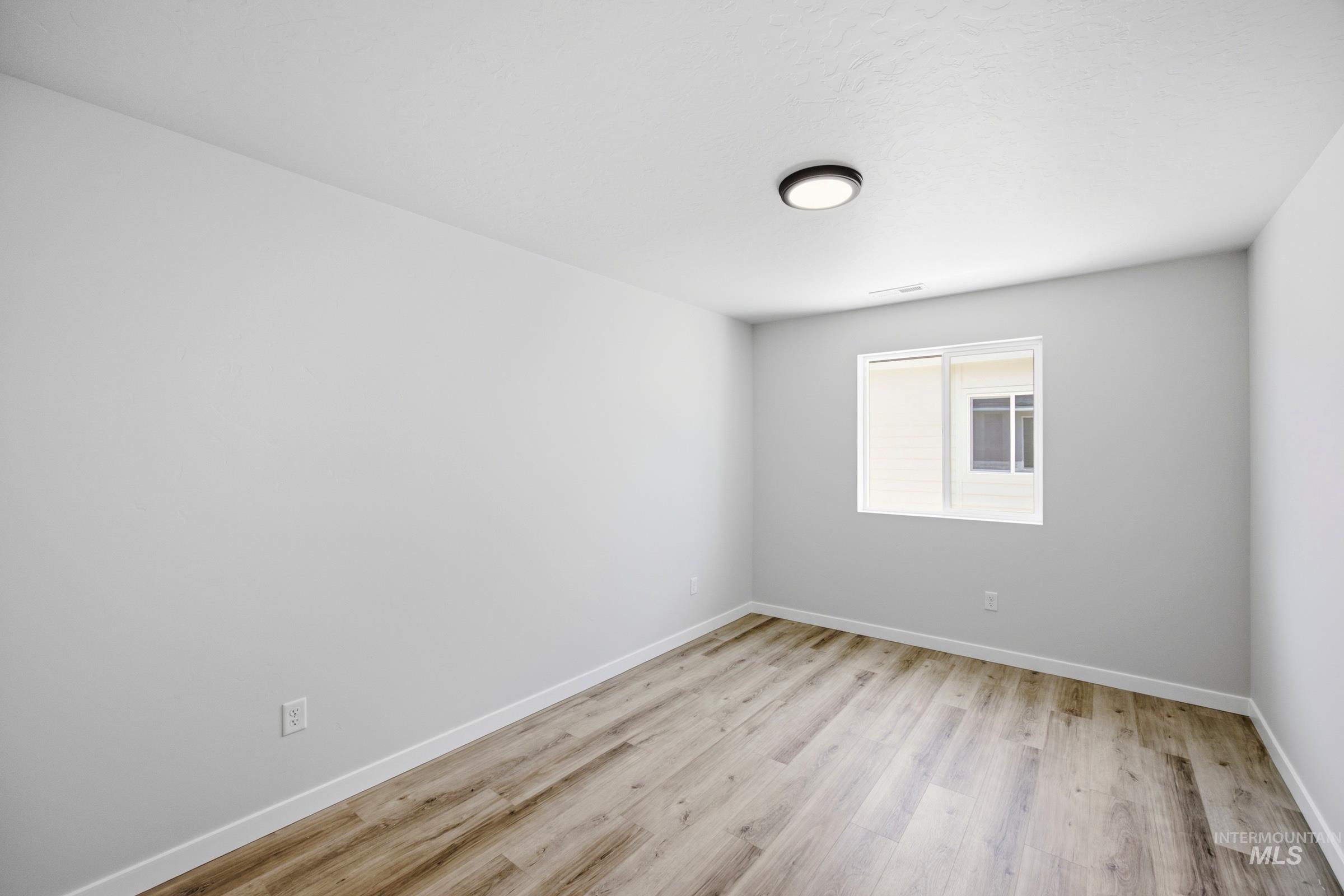 Bright interior space with wood-finish flooring, a contemporary flush-mount ceiling light, white baseboards, and a window with blinds