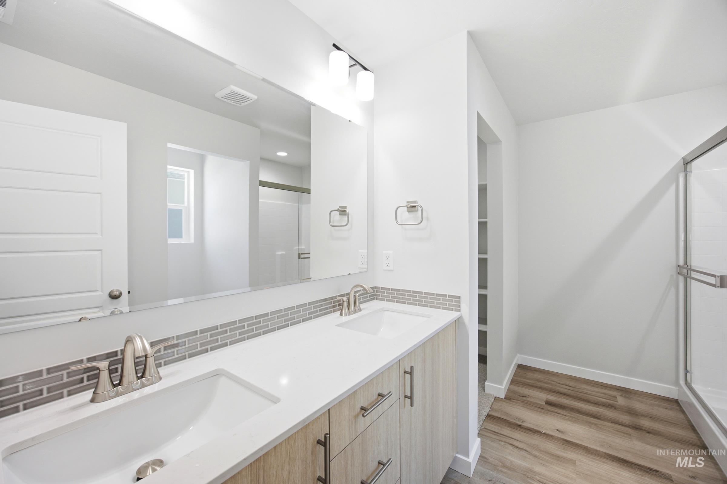 Bathroom featuring a dual vanity with light wood-finish cabinetry, white countertops, and a gray subway tile backsplash