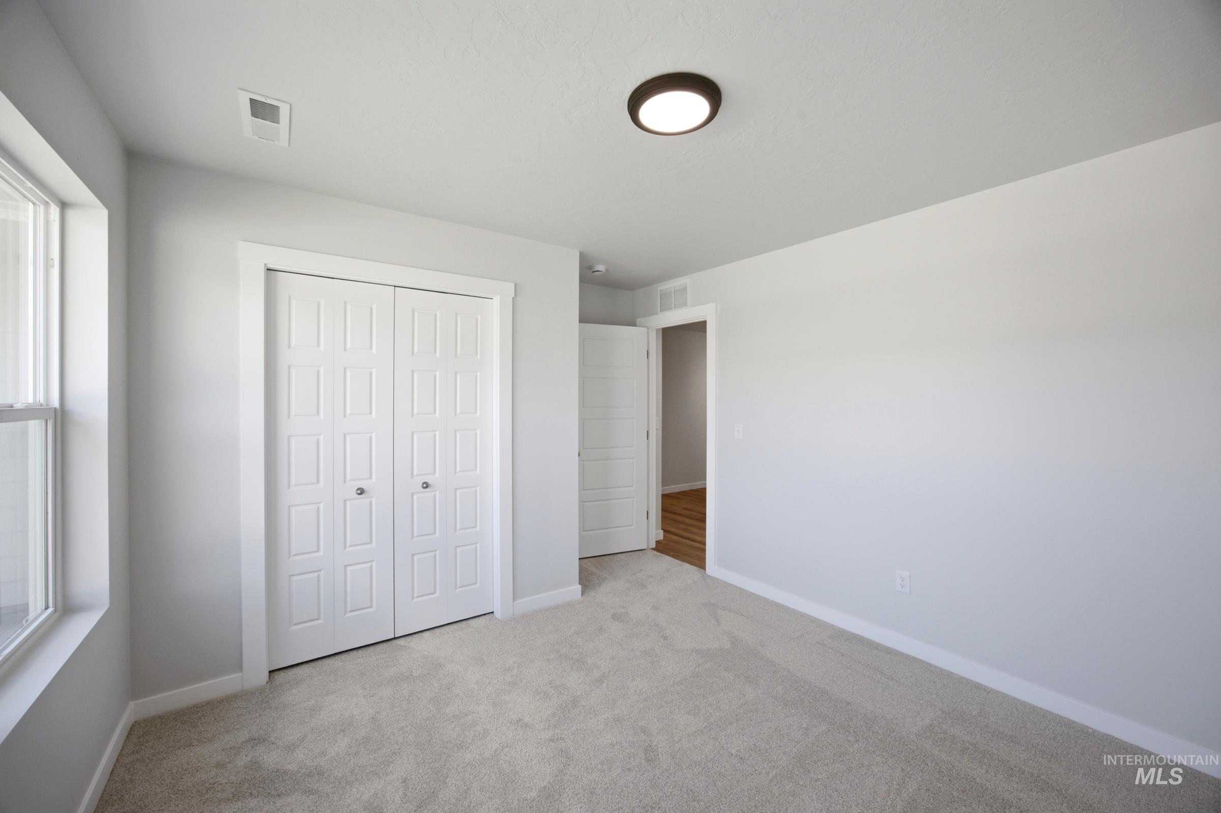 Carpeted room featuring a double-pane window, white bi-fold closet doors with panel detailing, a flush-mount ceiling light fixture, and light gray wall paint