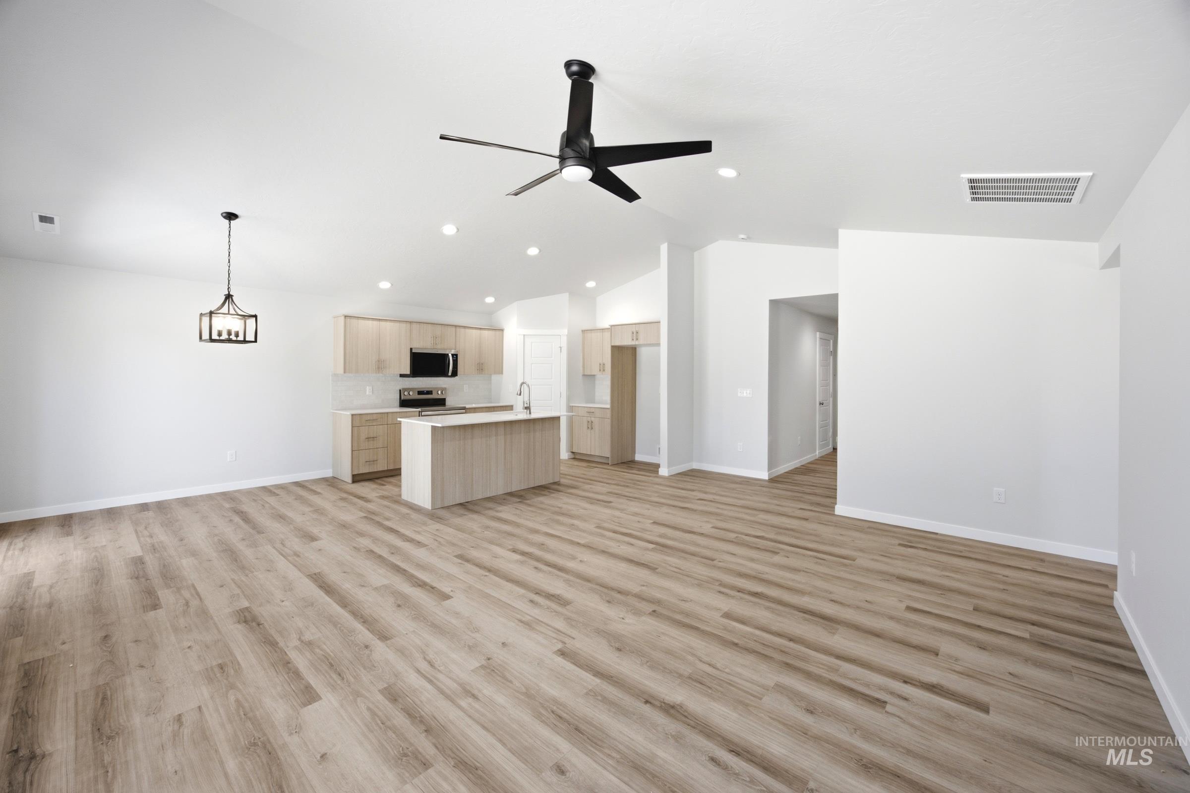 Open-concept living area featuring vaulted ceilings, wood-finish flooring, and a modern ceiling fan