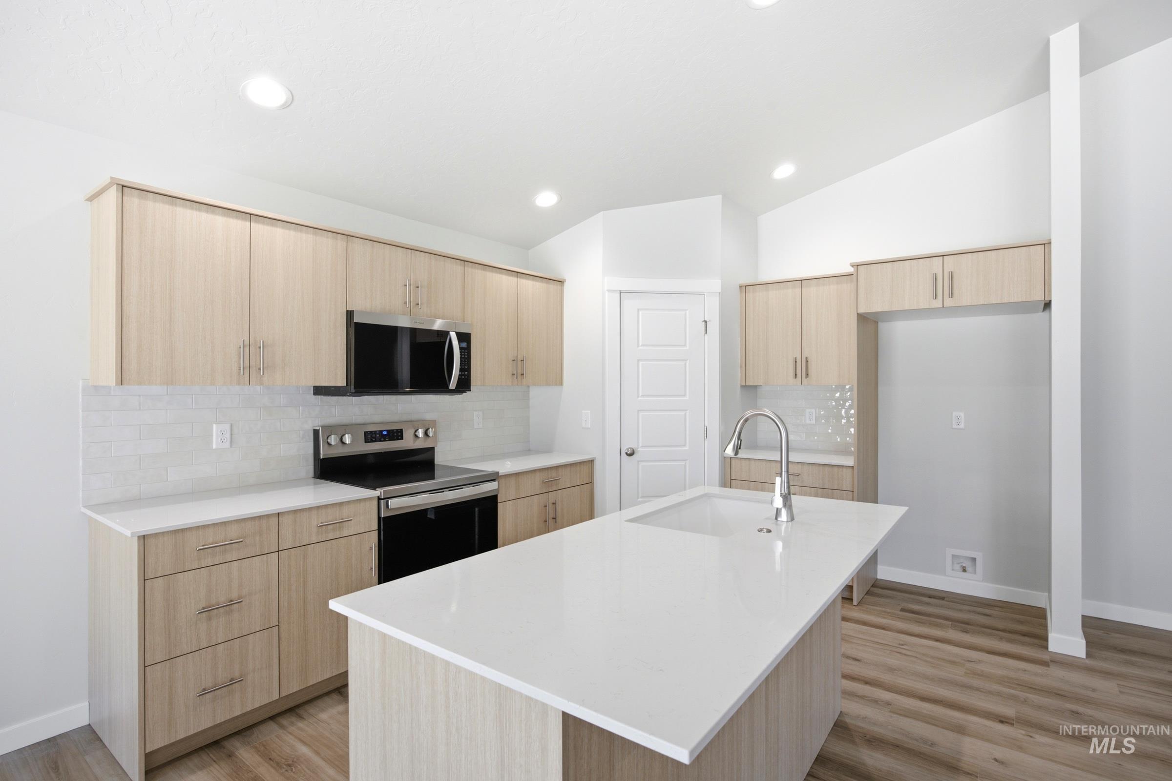 Modern kitchen featuring light wood-finish cabinetry, white countertops, and stainless steel appliances