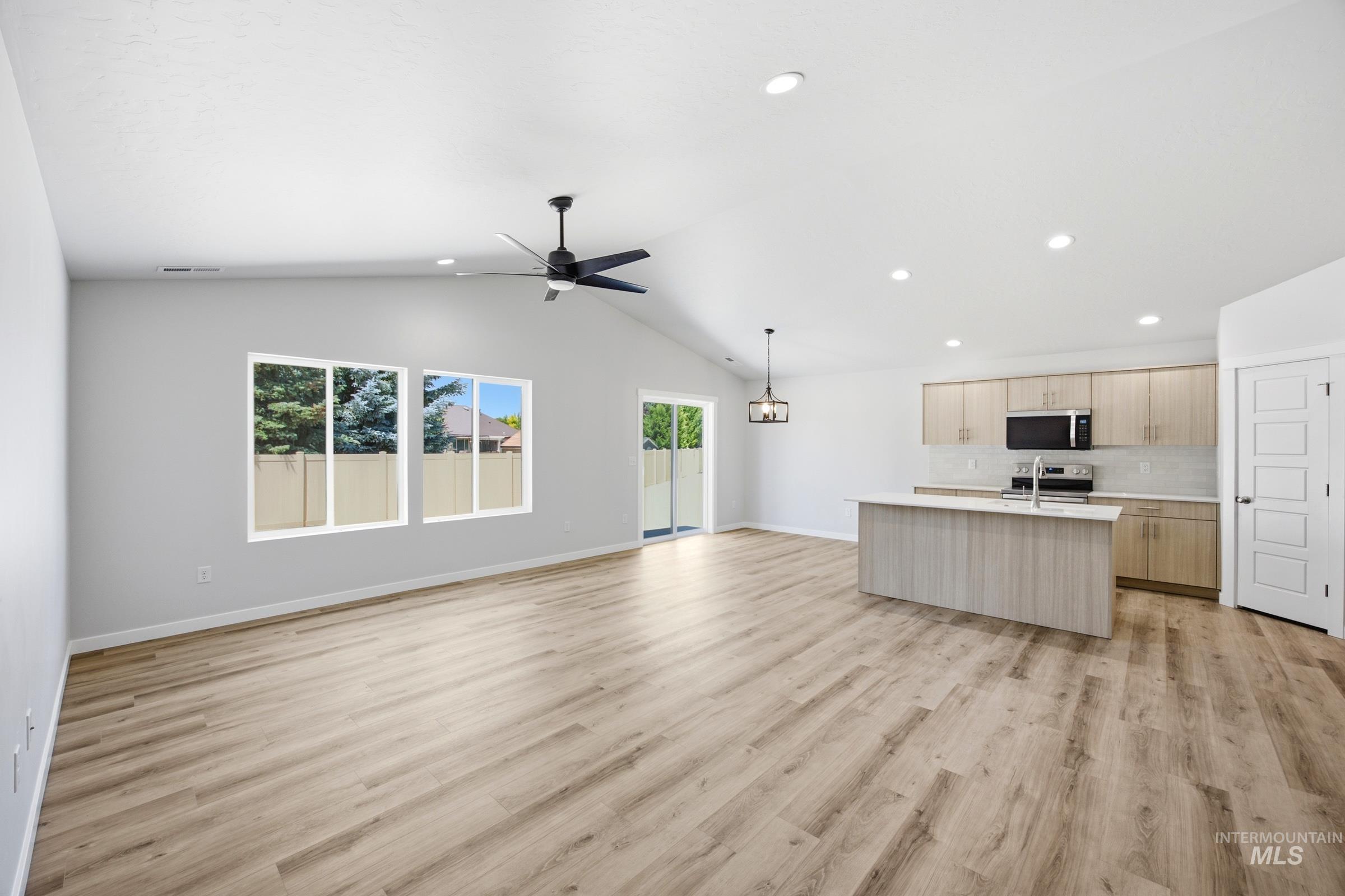Open-concept living area featuring vaulted ceilings, wood-finish flooring, a modern kitchen island with seating, stainless steel appliances, and a sliding glass door for outdoor access