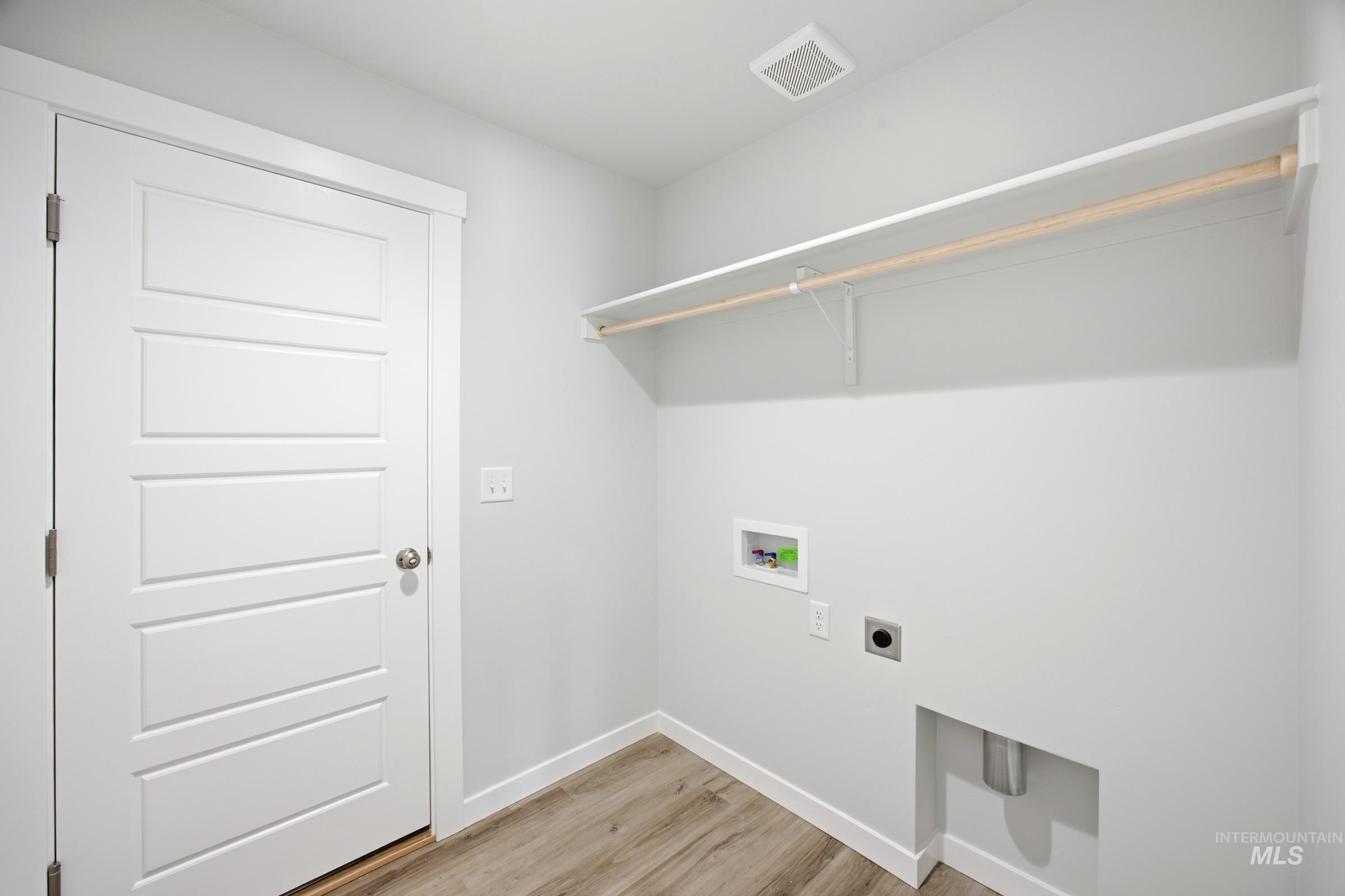 Utility room featuring wood-finish flooring, white trim, and a white interior door with panel detailing