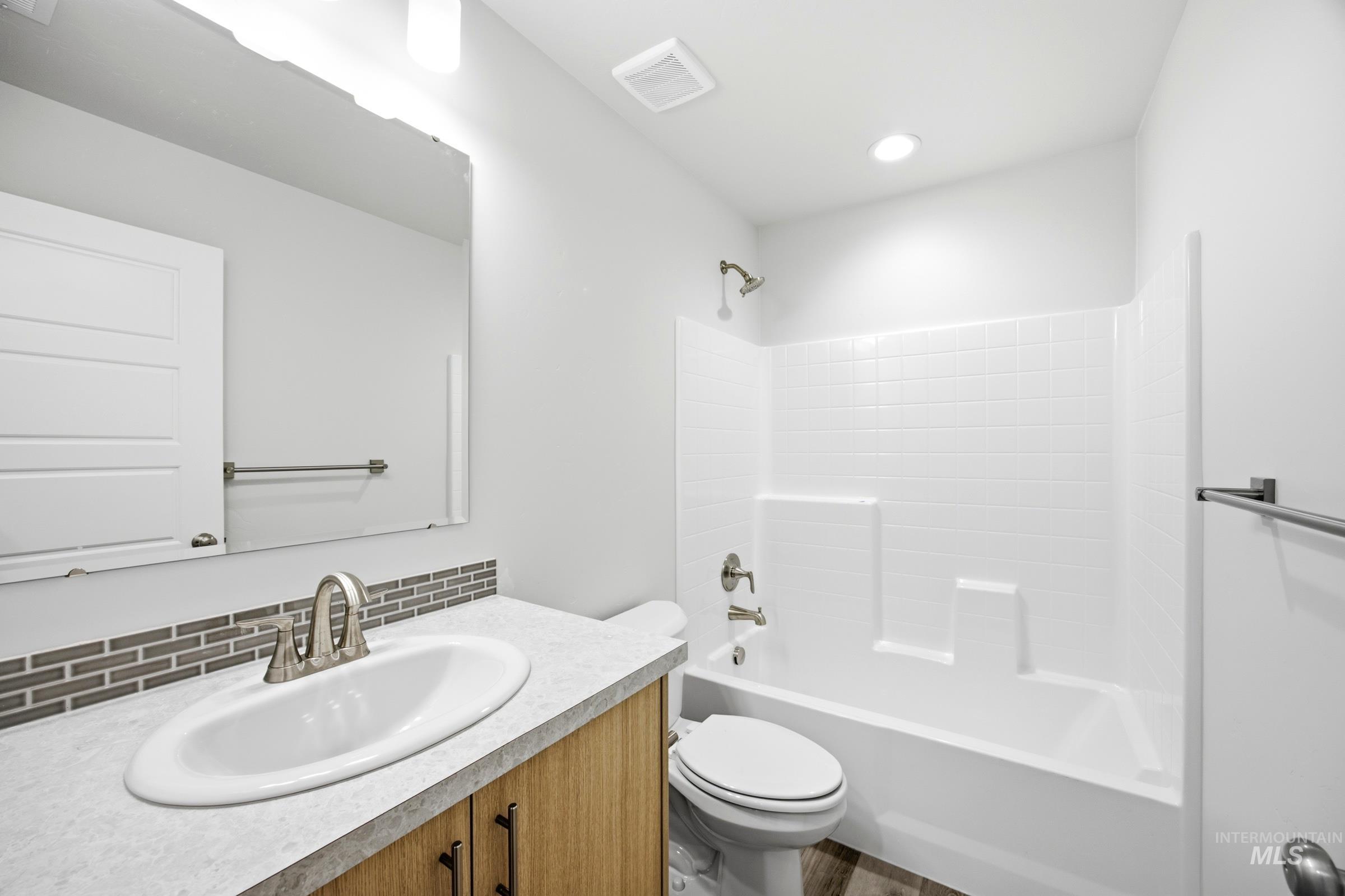Bathroom featuring wood-finish vanity with dark hardware, white oval undermount sink, and a gray-toned mosaic tile backsplash