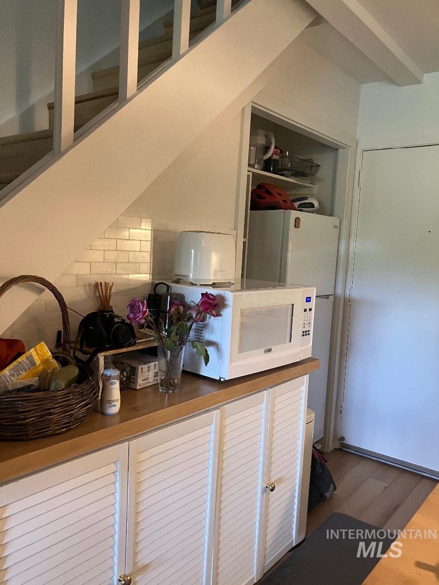 White louvered cabinetry with gold-tone hardware, a wood-finish countertop, and white subway tile backsplash