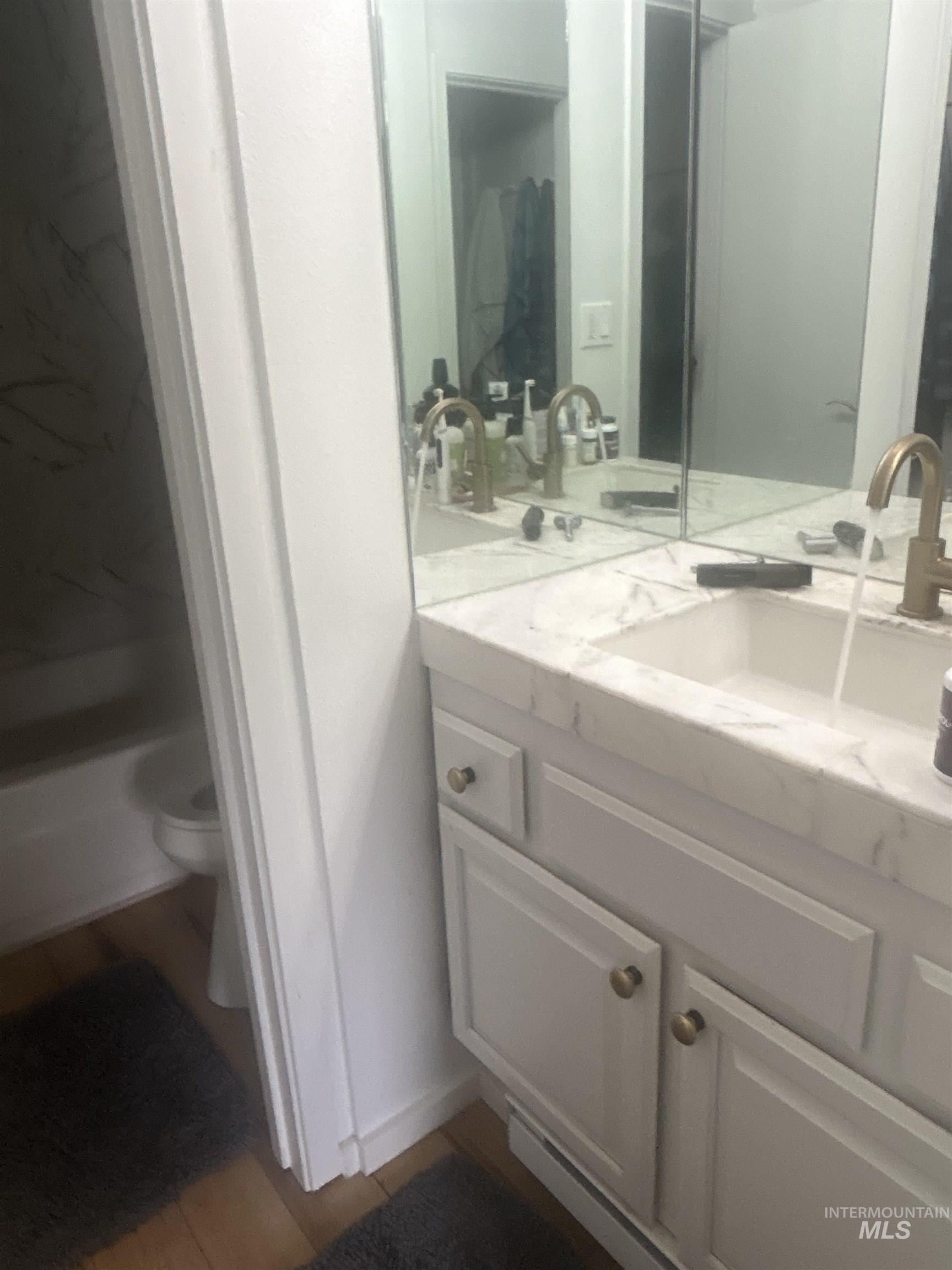 White vanity featuring a single basin, brass-finish faucet, and a light-toned countertop
