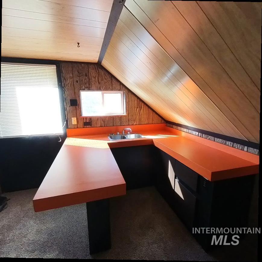 Unfurnished office with wood walls, lofted ceiling, wooden ceiling, and dark colored carpet