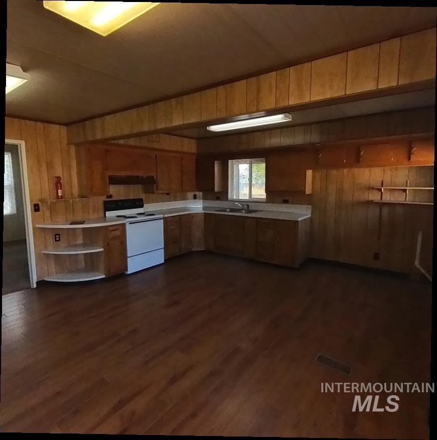 Kitchen with wood walls, white electric range oven, light countertops, dark wood-type flooring, and open shelves