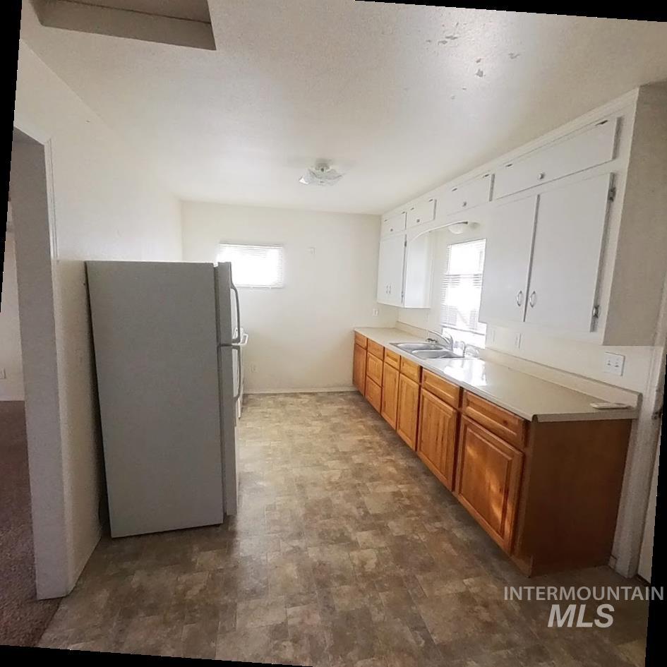 Kitchen featuring freestanding refrigerator, brown cabinetry, light countertops, and white cabinets