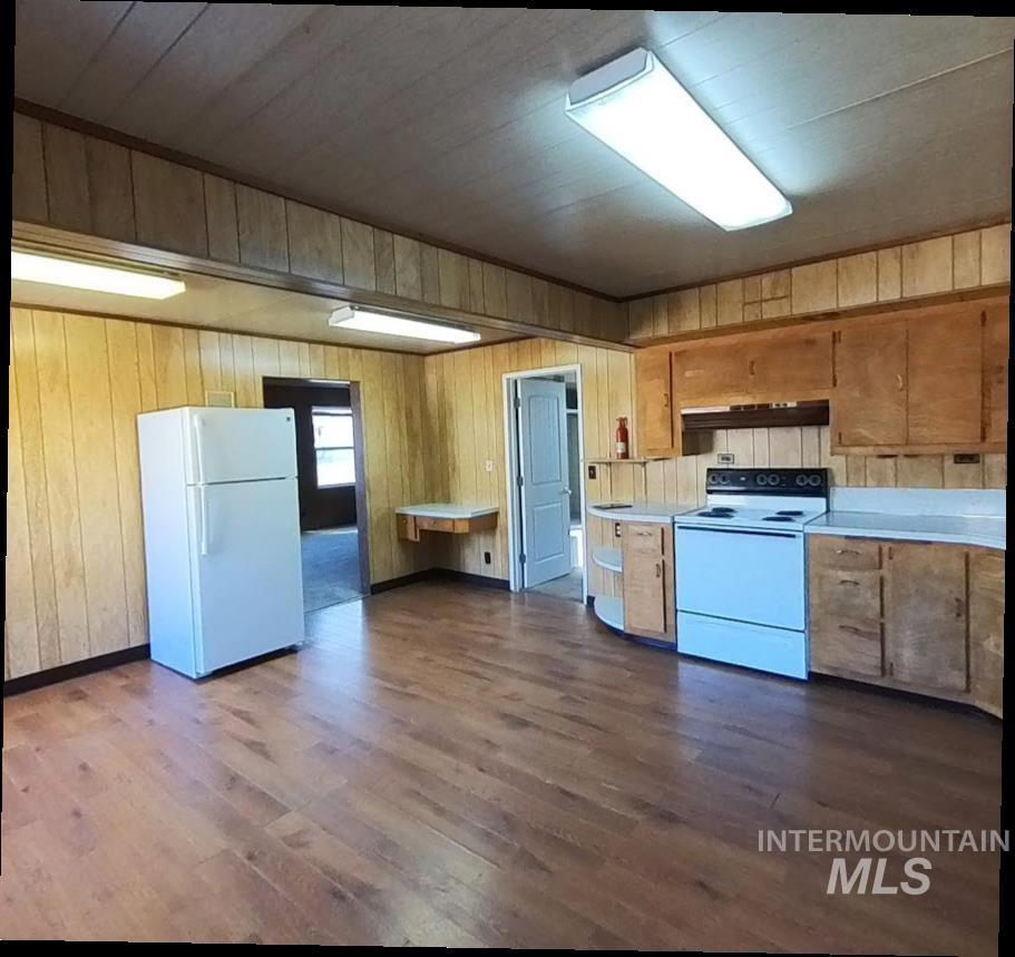 Kitchen with light countertops, white appliances, dark wood-style floors, wood walls, and under cabinet range hood