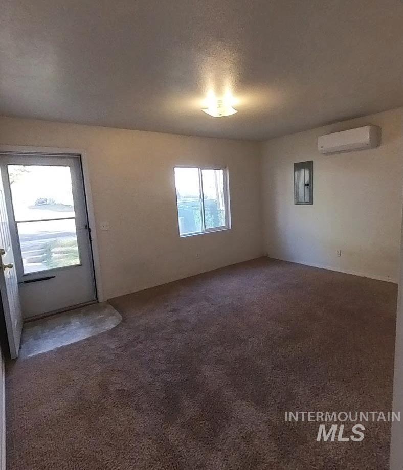 Unfurnished room featuring dark carpet, a textured ceiling, electric panel, and a wall mounted air conditioner