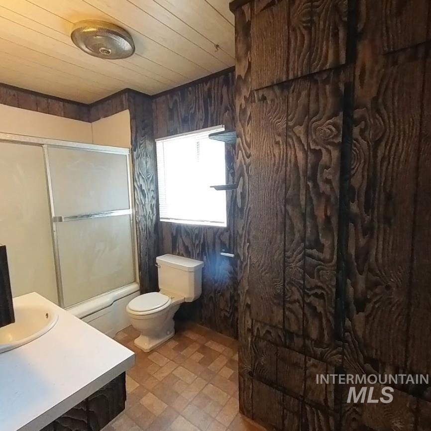 Full bath with enclosed tub / shower combo, vanity, wood ceiling, and wood walls